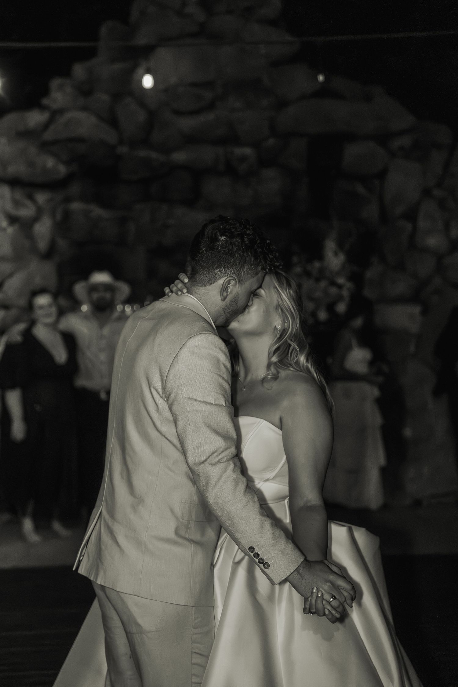 Black and white photo of a bride and groom sharing their first dance kiss at a romantic wedding reception.