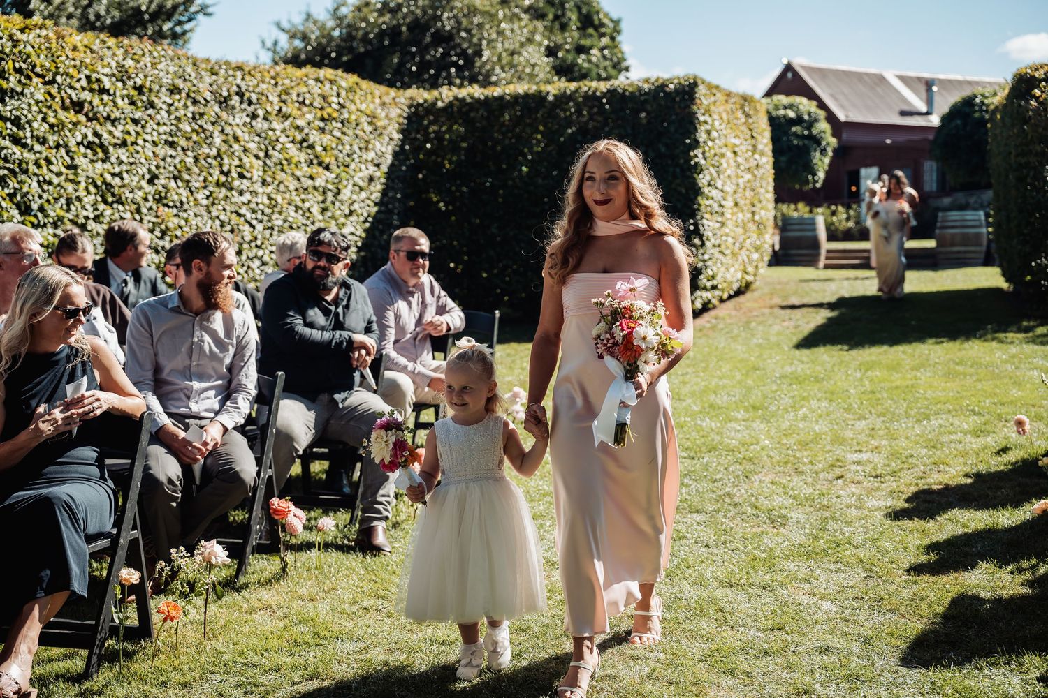 Bridesmaid in blush dress walking flower girl down the aisle at an outdoor garden wedding.