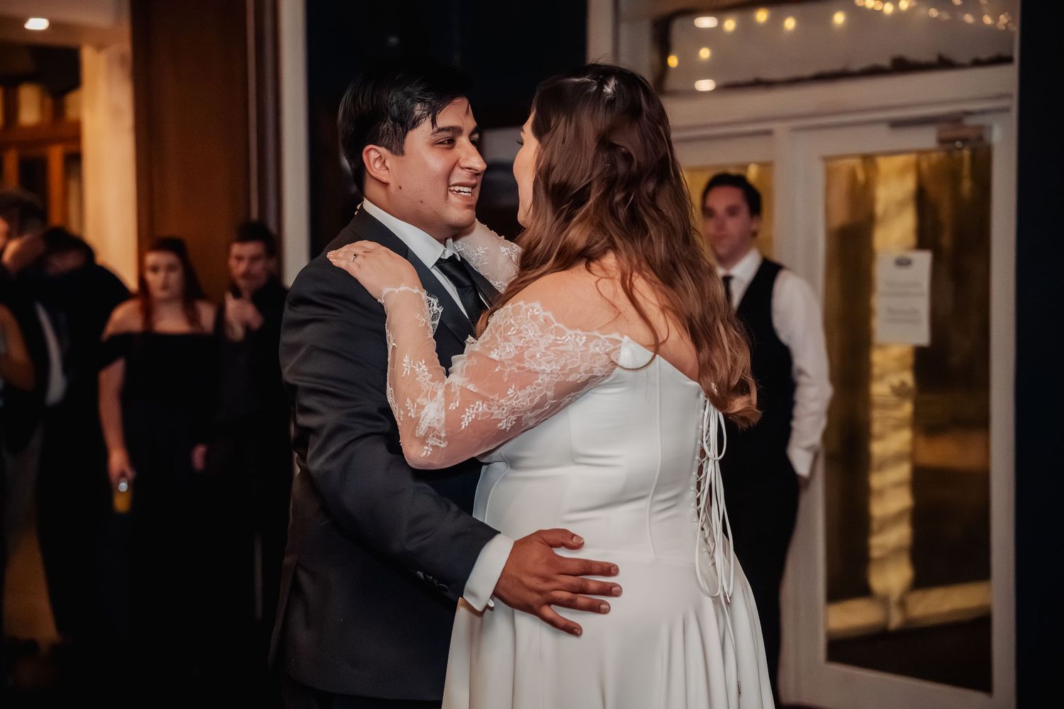 A romantic first dance at an indoor wedding reception with twinkling lights in the background.