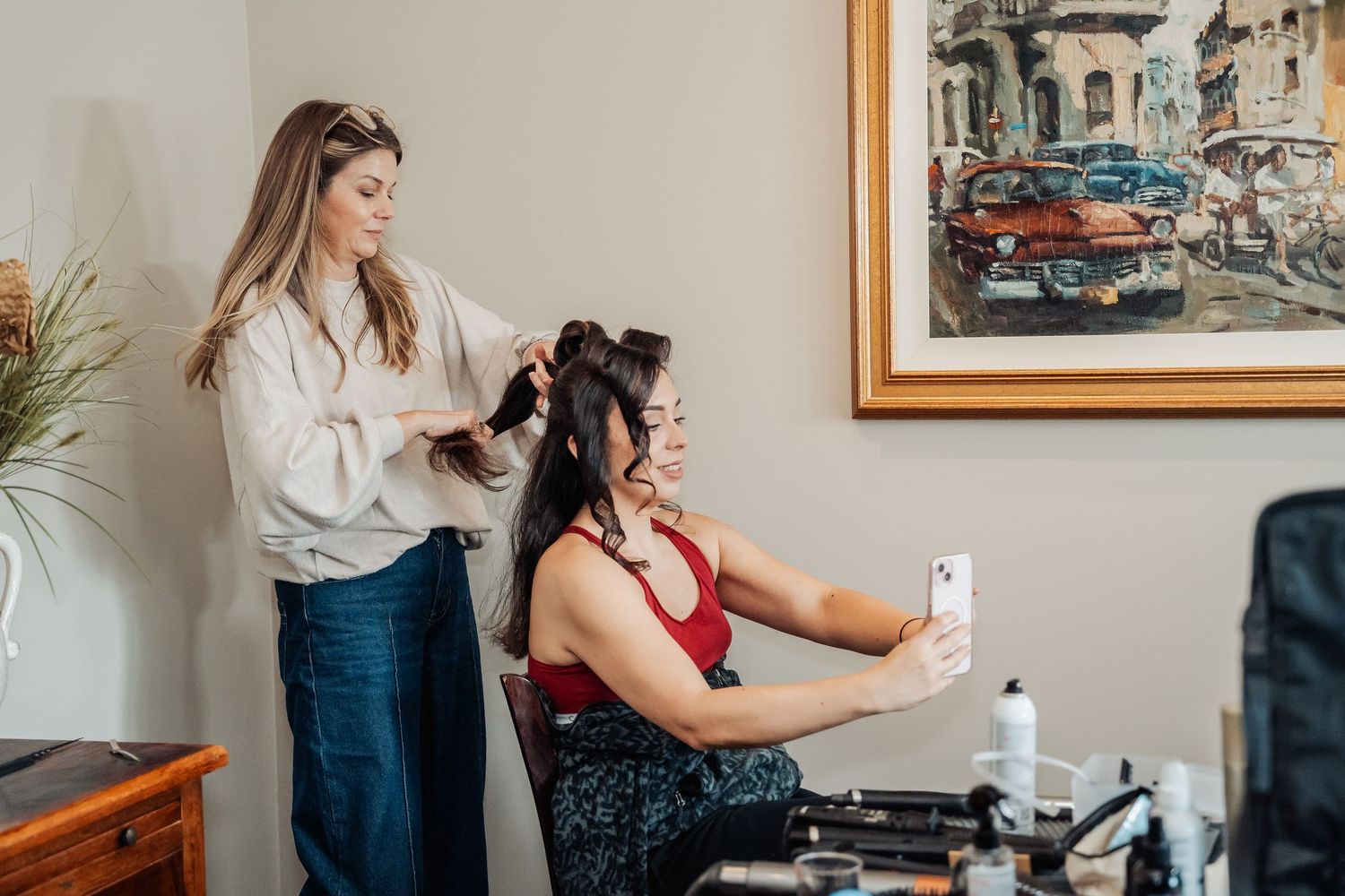 Stylist working on a client's hair in a salon with vintage artwork of classic cars hanging on the wall.