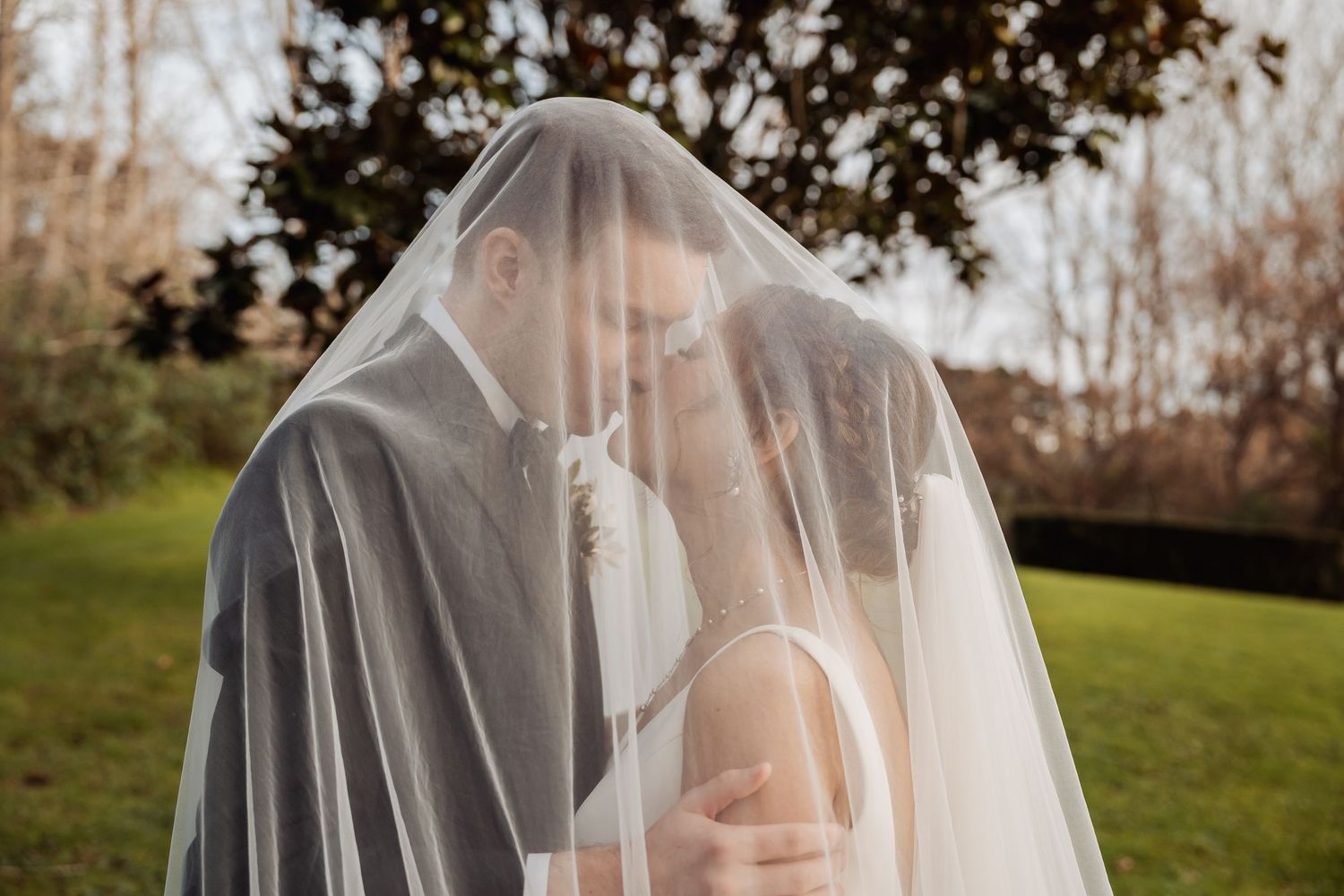 A romantic moment captured under a sheer wedding veil in an outdoor garden setting.