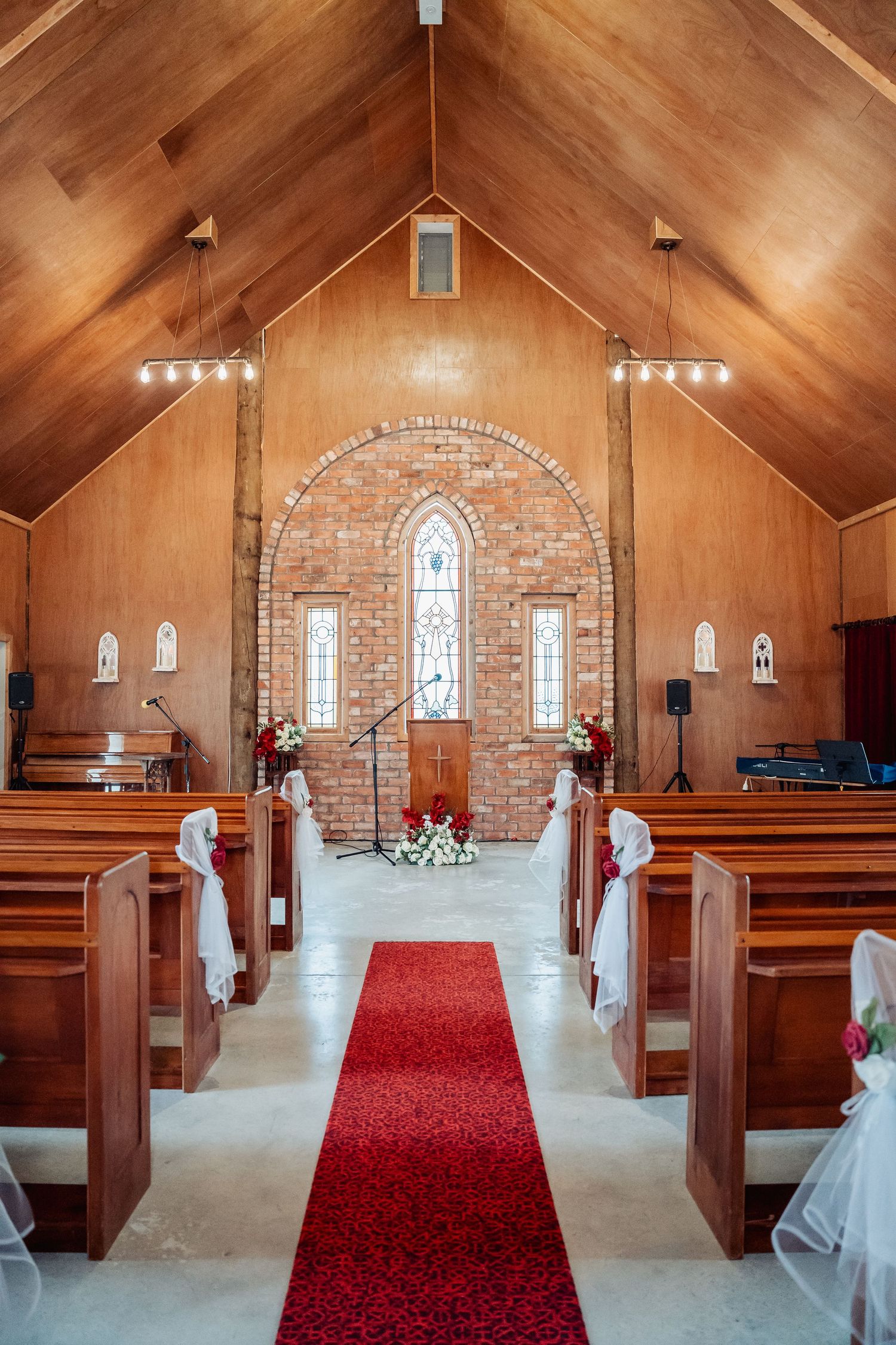 Elegant church interior with red petal aisle, wooden pews, and brick altar wall for wedding ceremony.