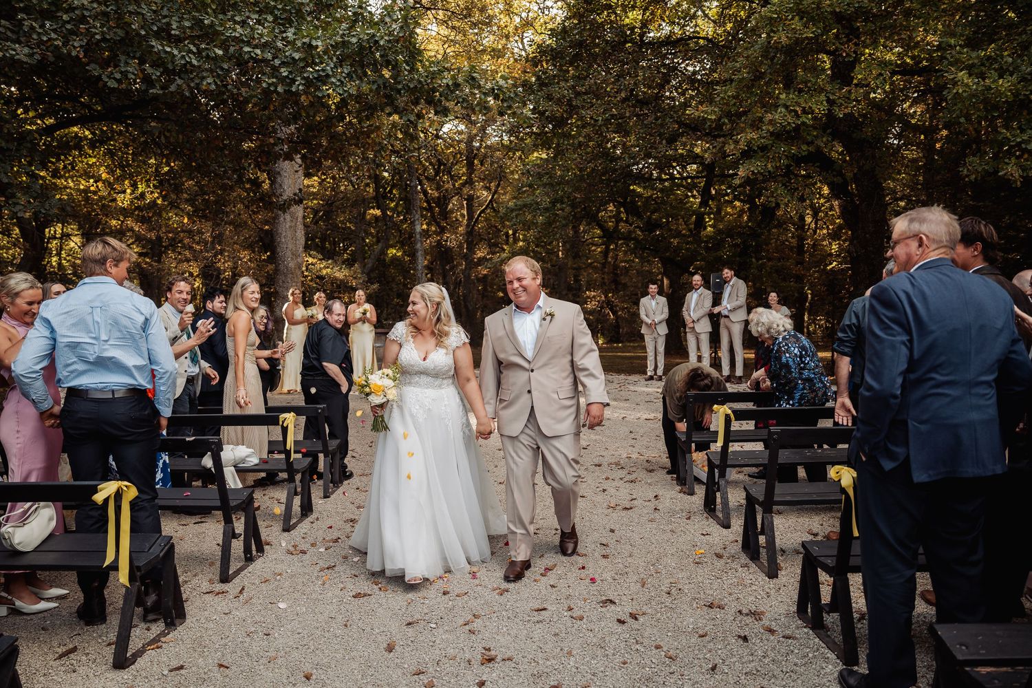 Newlyweds walking back down the aisle after outdoor woodland wedding ceremony with guests.