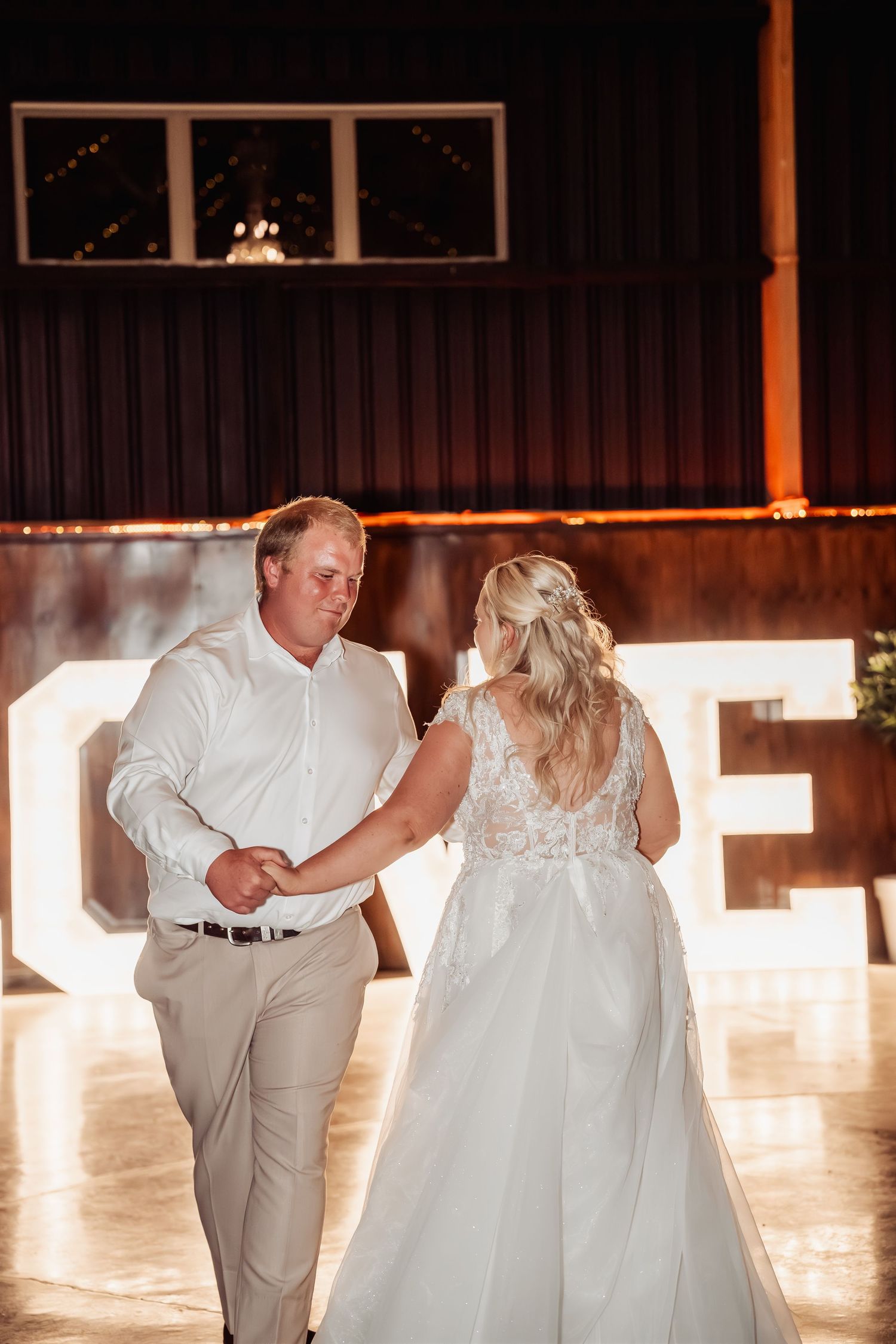 Bride and groom share their first dance in front of illuminated LOVE letters at reception.