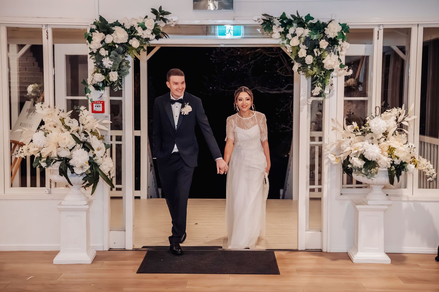 Indoor wedding ceremony setup with white floral arch and elegant decor.