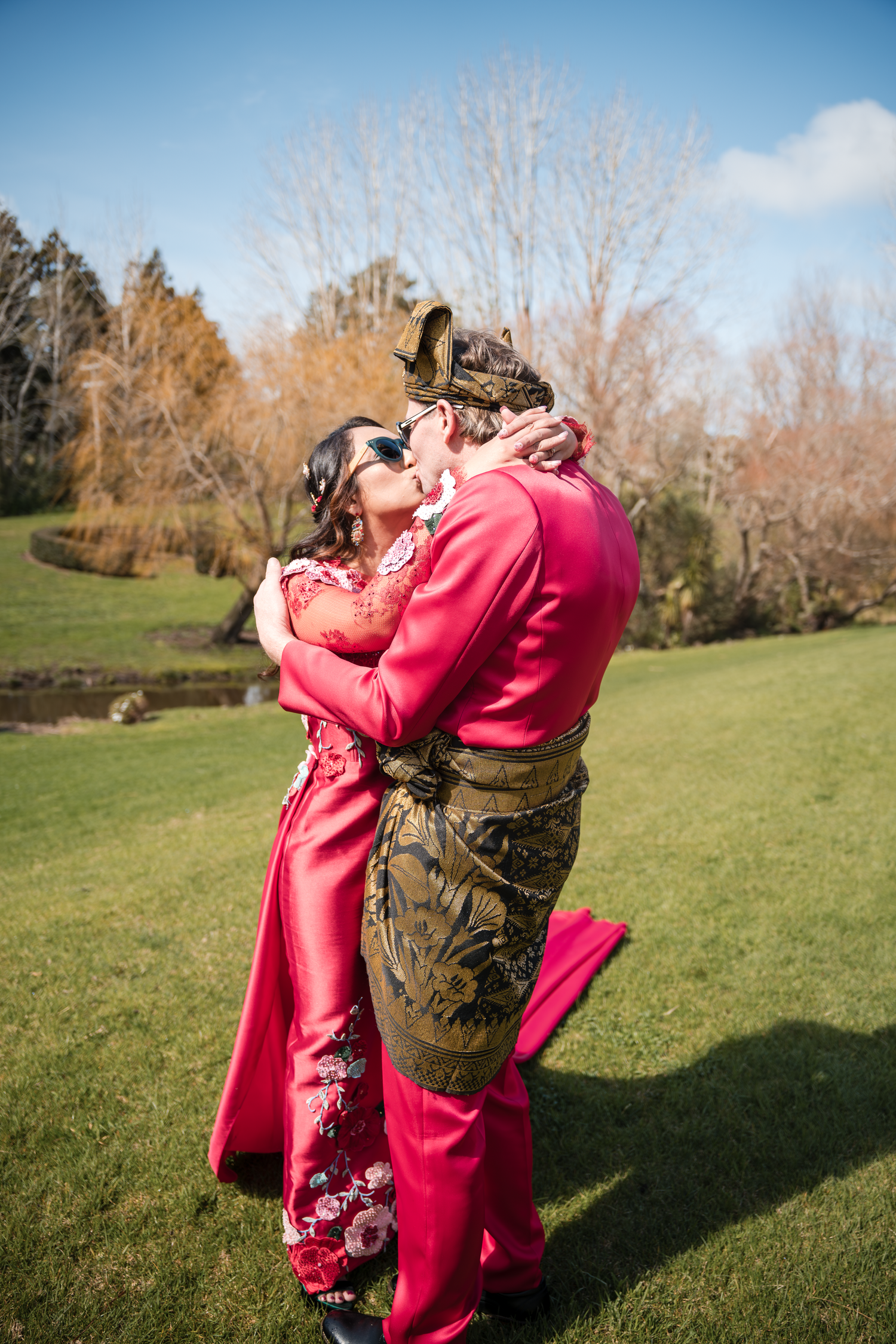 Intimate moment between couple in pink formal wear embracing on green lawn.