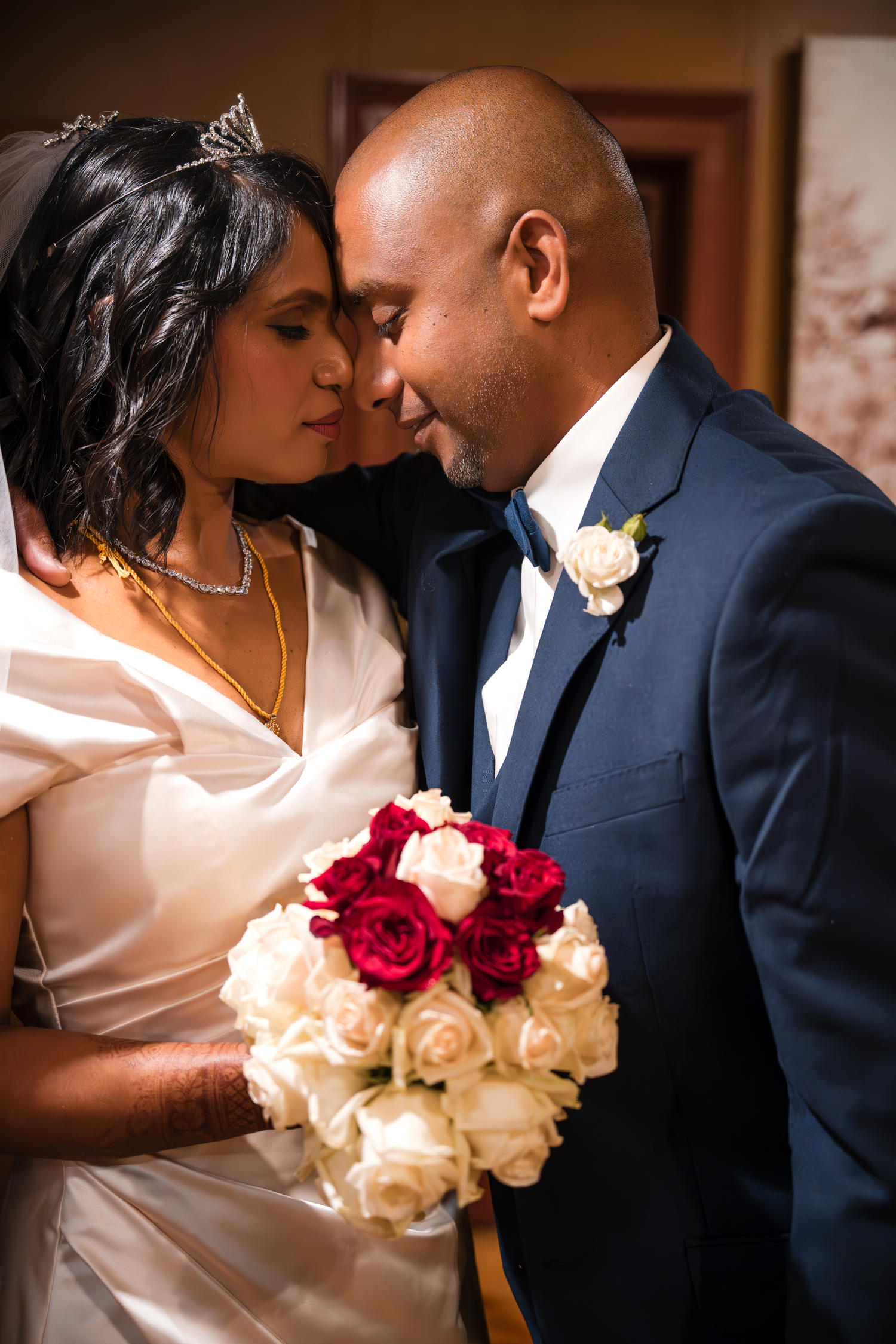 A romantic wedding portrait shows a couple in an intimate moment with a red and white rose bouquet.