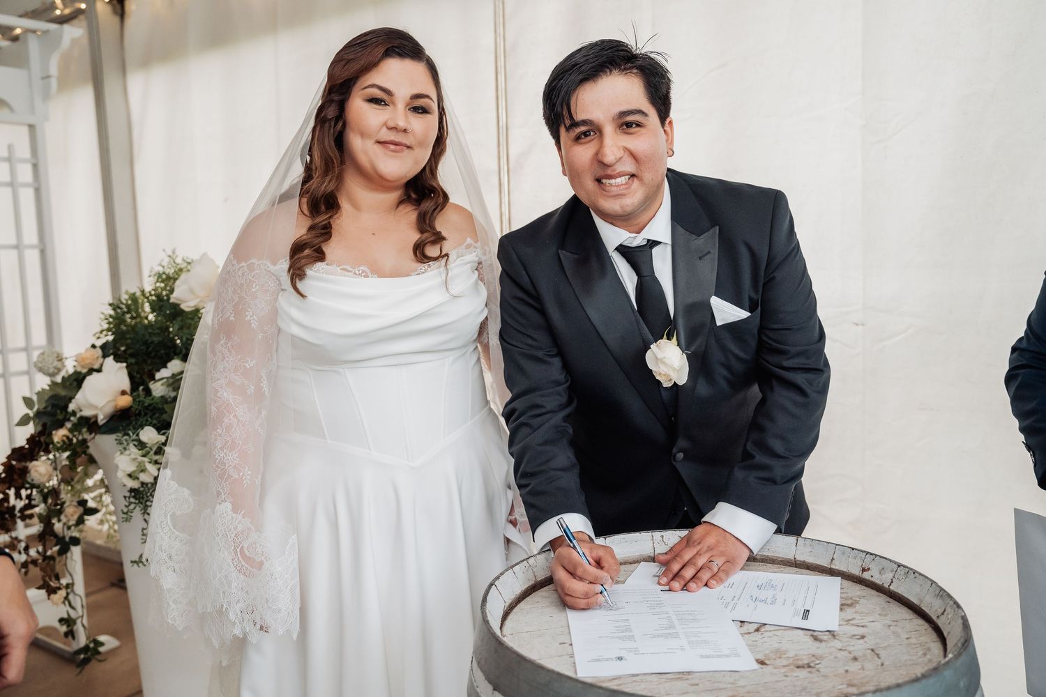 Happy newlyweds sign marriage documents at an elegant indoor ceremony with vintage decor.