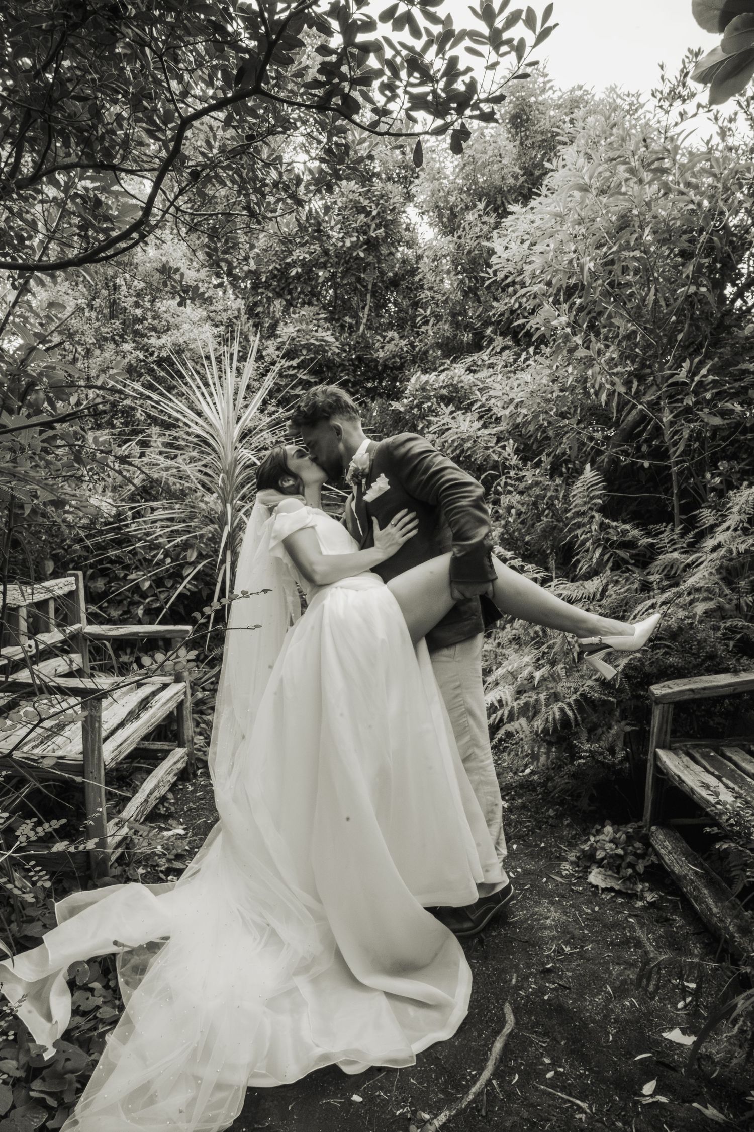 Black and white photo of bride and groom sharing a romantic dip kiss in a lush garden setting.