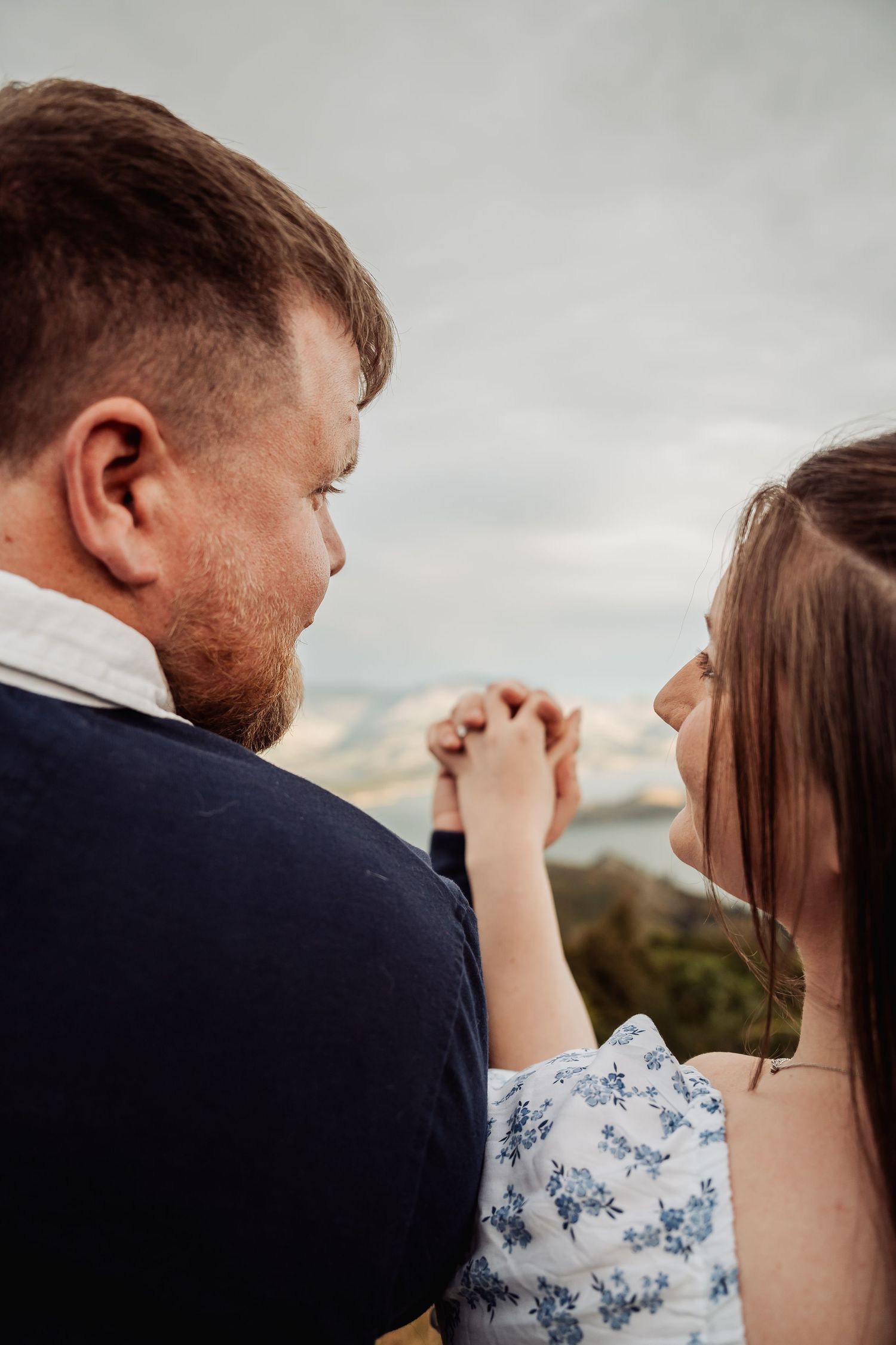 Couple holding hands tenderly with scenic mountain backdrop on a cloudy day.