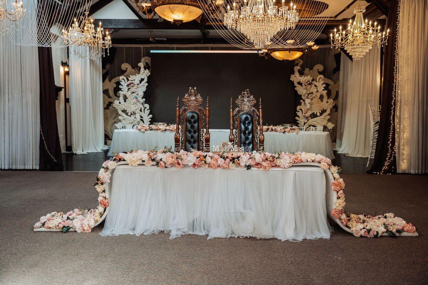 Elegant ballroom with crystal chandeliers and white draped tables for a wedding reception.