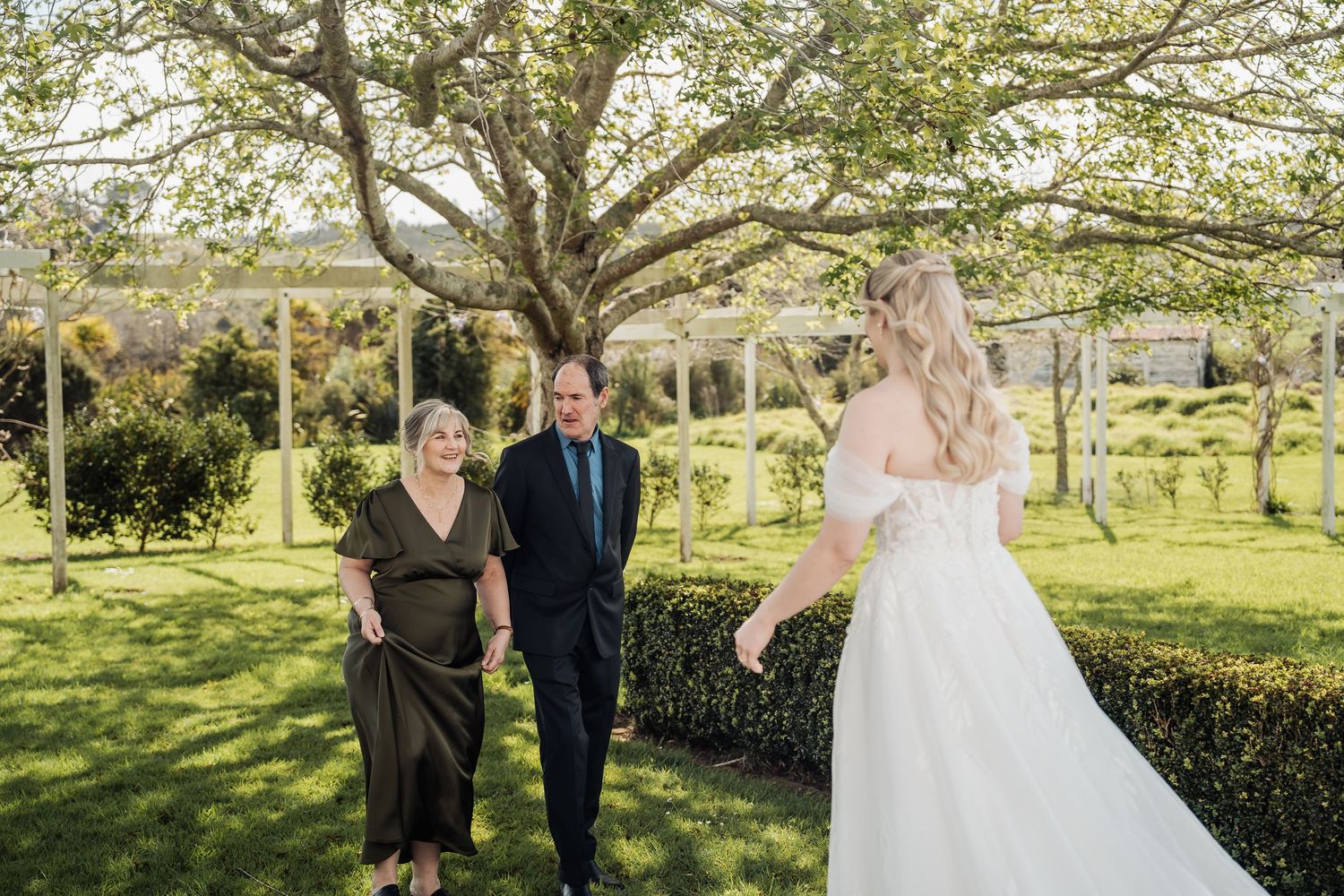 Wedding party gathers under blooming trees in a lush garden setting.