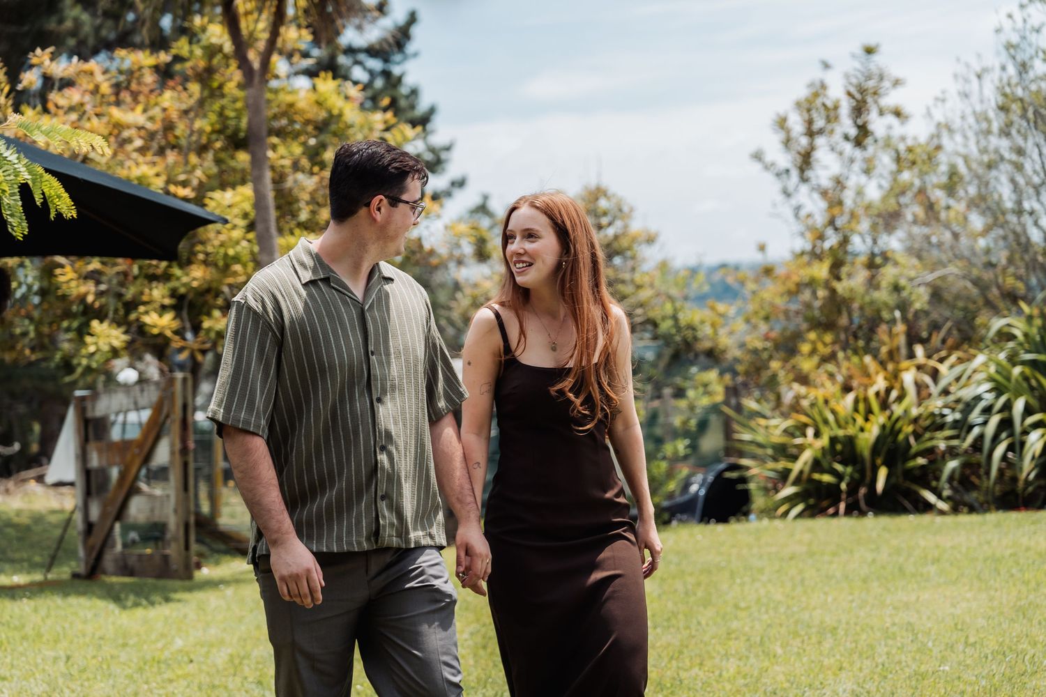 Happy couple holding hands and walking through a sunny garden on their wedding day.