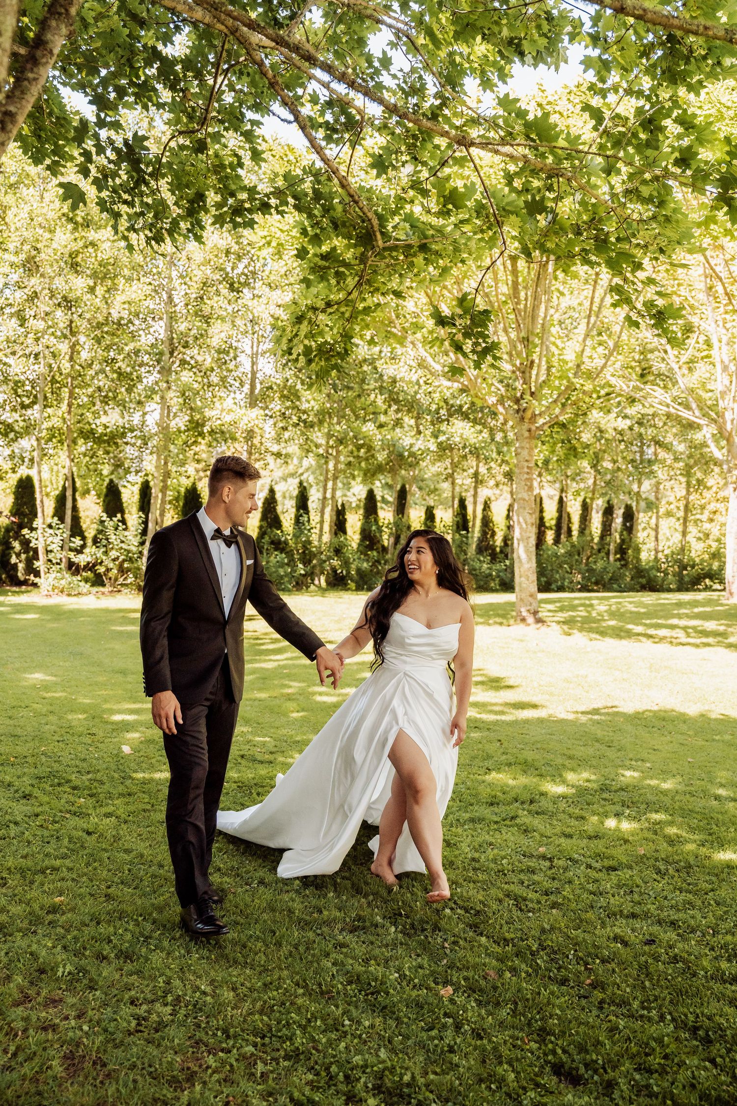 Bride and groom hold hands walking through lush green garden on their wedding day.