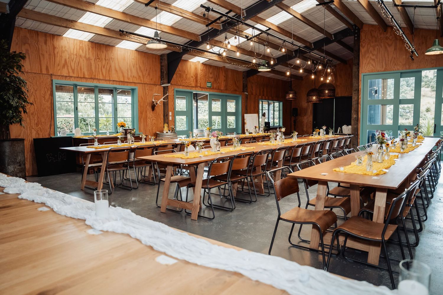 Rustic wedding reception hall with long wooden tables set for a dinner celebration.
