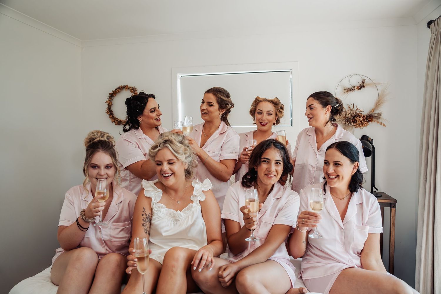 Bride and bridesmaids in pink robes celebrating with champagne glasses indoors.