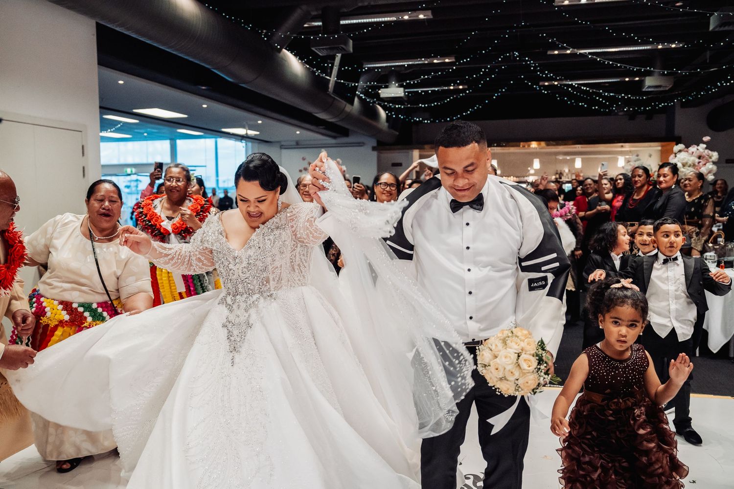 A large group of wedding guests dancing and celebrating together on a dark dance floor.