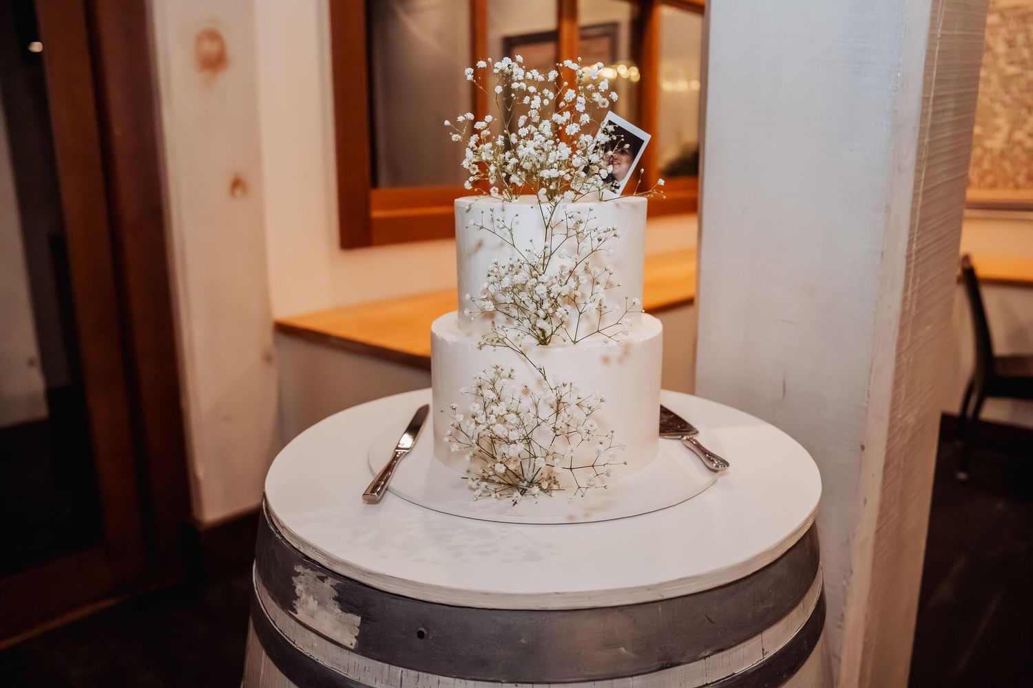 Three-tiered white wedding cake decorated with delicate flowers sits on silver display stand.