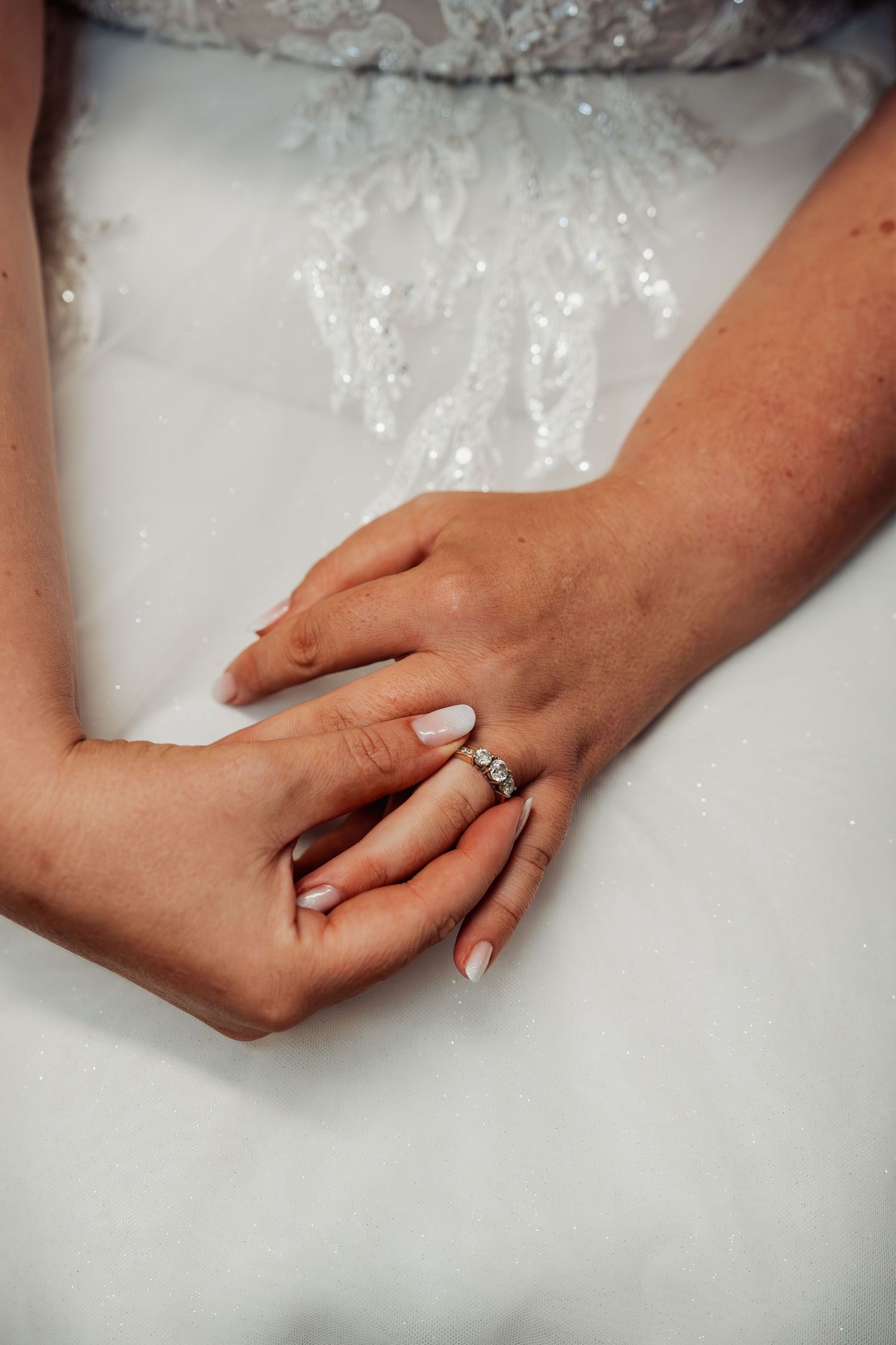 Close-up of bride's hands showing diamond wedding ring on white lace wedding dress.