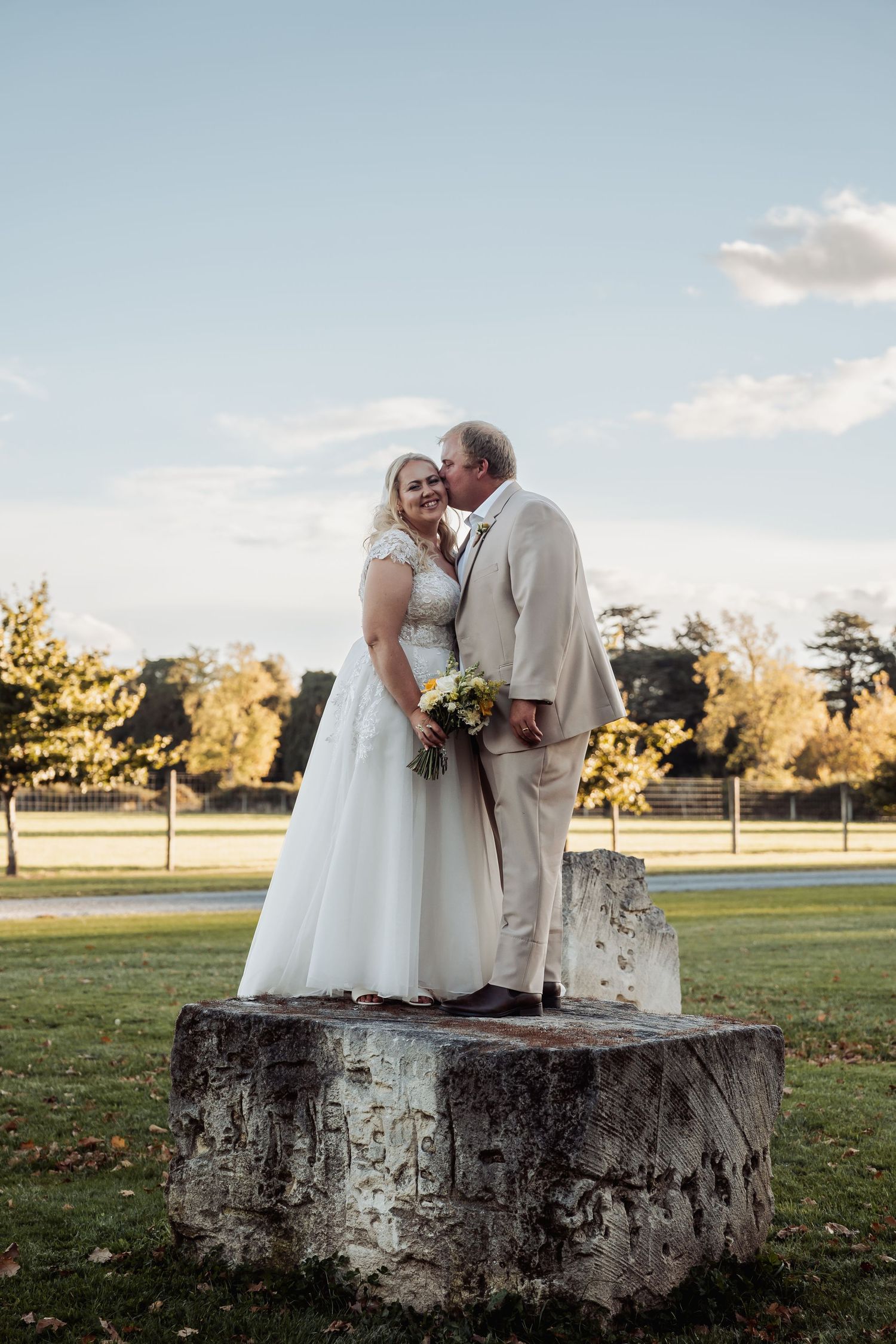 Bride and groom posing on large stone block in golden hour light.