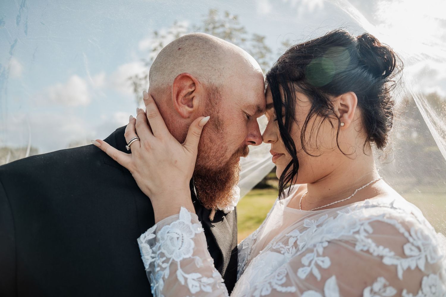 A couple shares an intimate moment in their wedding attire against a sunlit background.