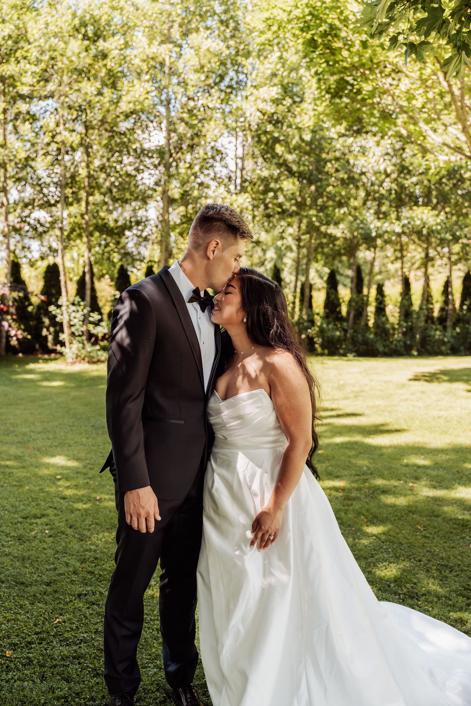 Bride and groom share a tender kiss in a lush green garden on their wedding day.