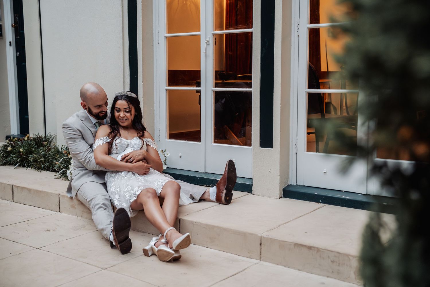 Bride and groom sit relaxed on venue steps sharing a joyful intimate moment together.
