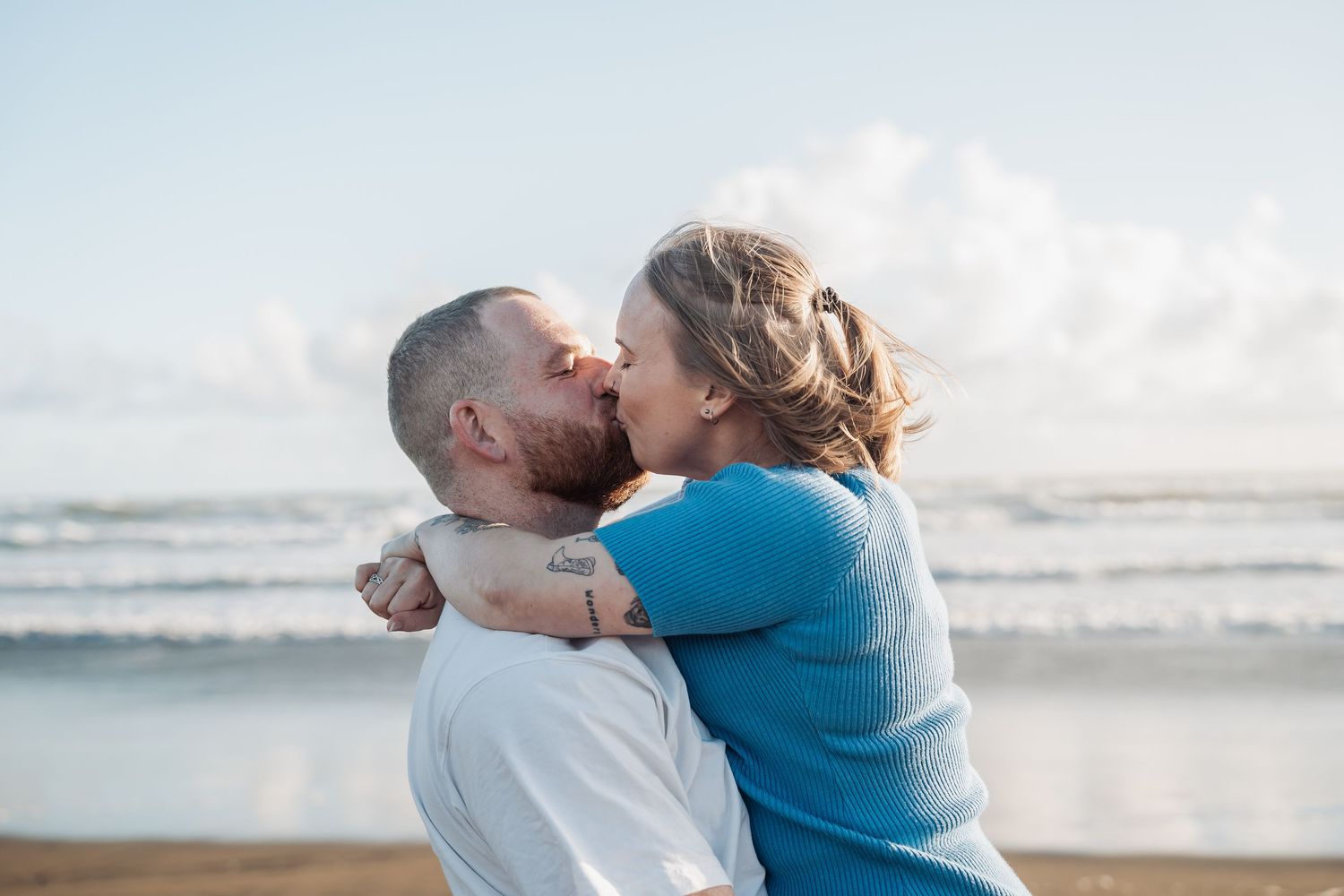 An intimate embrace shared between a couple on a sandy beach with ocean waves in the distance.