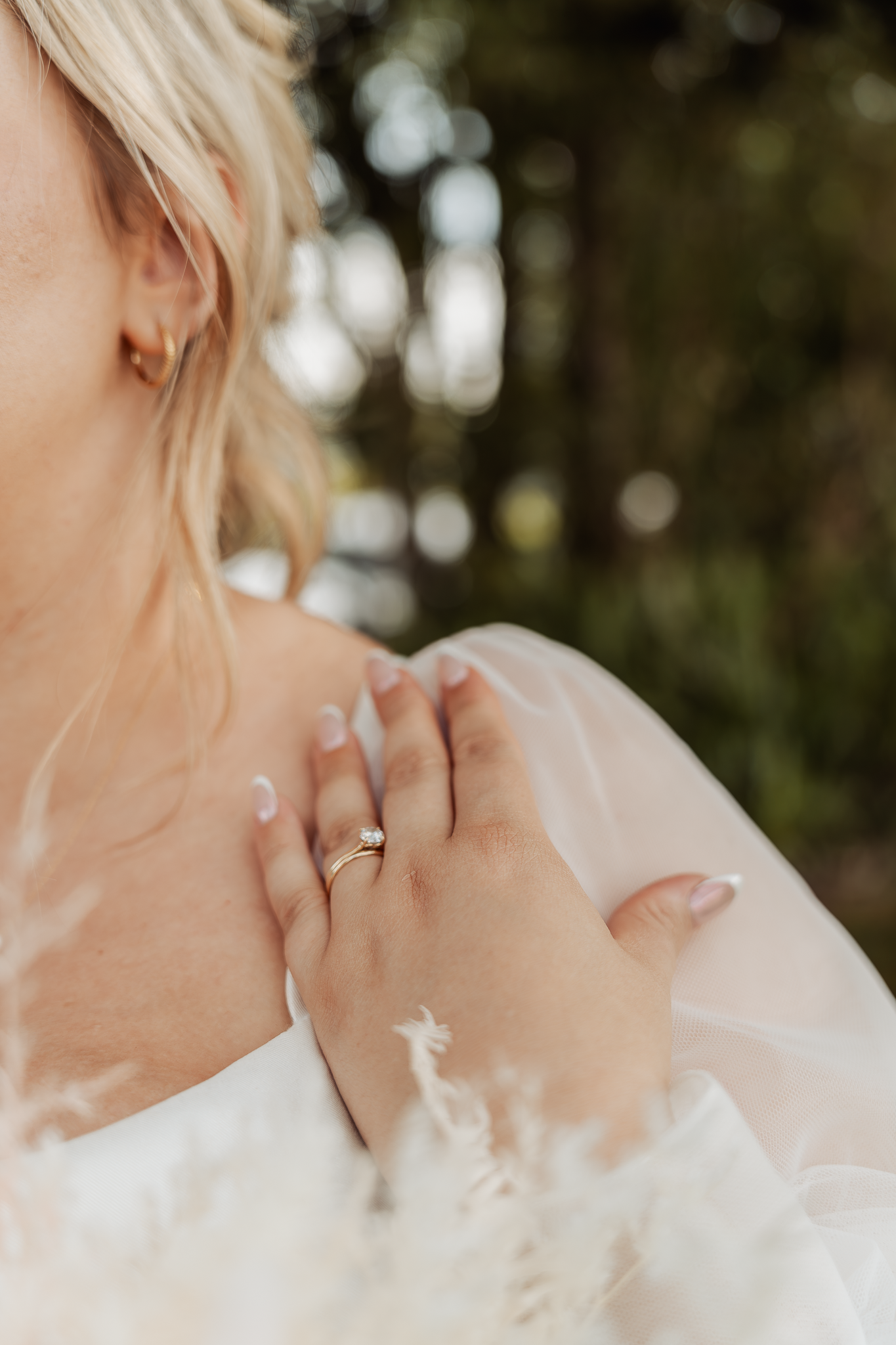 Close-up shot of a bride's hand with wedding ring against delicate white lace and tulle fabric in natural lighting.