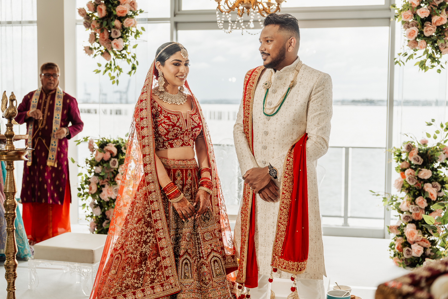 A couple stands together during their traditional Indian wedding ceremony surrounded by floral decorations.