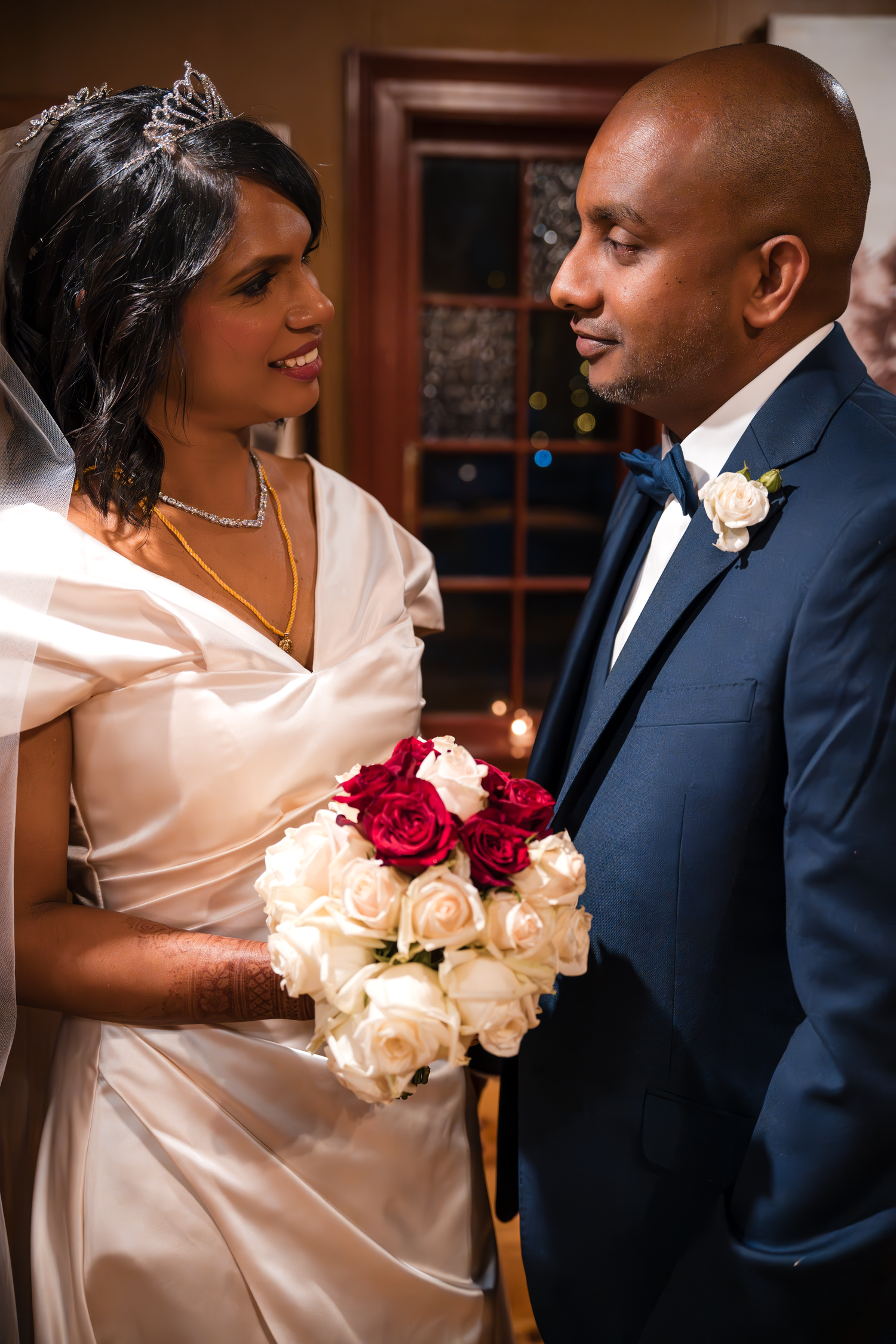 A couple shares an intimate moment while holding a bouquet of red and cream roses at their wedding.