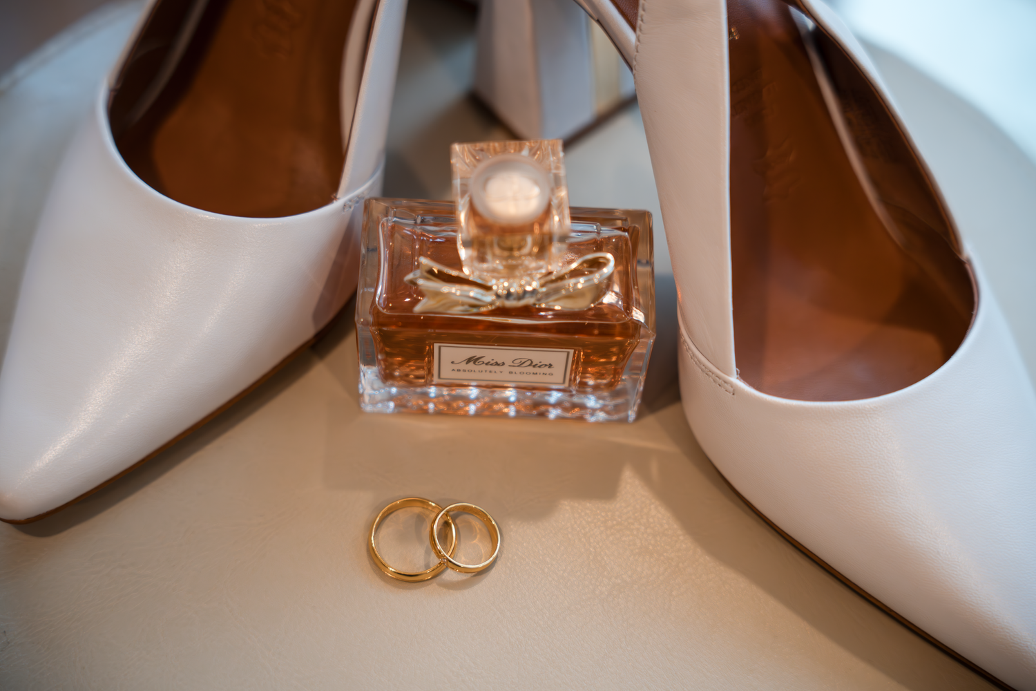 Wedding details with white bridal shoes, perfume bottle and gold wedding rings.