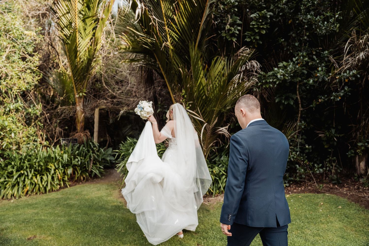 Couple walking through a garden setting with palm trees and natural greenery.