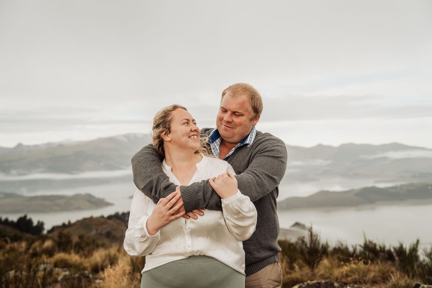 A couple shares a joyful moment on a mountaintop overlook with misty valleys and mountains in the background.