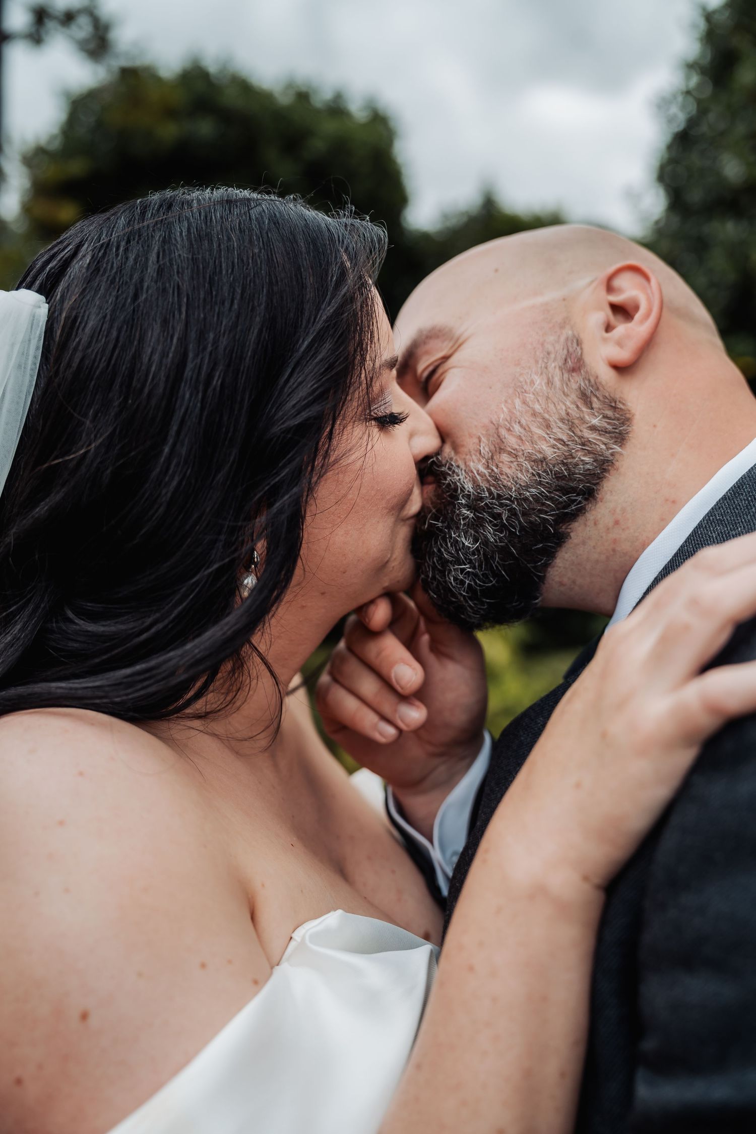 Bride and bald bearded groom share a romantic first kiss at their outdoor wedding.