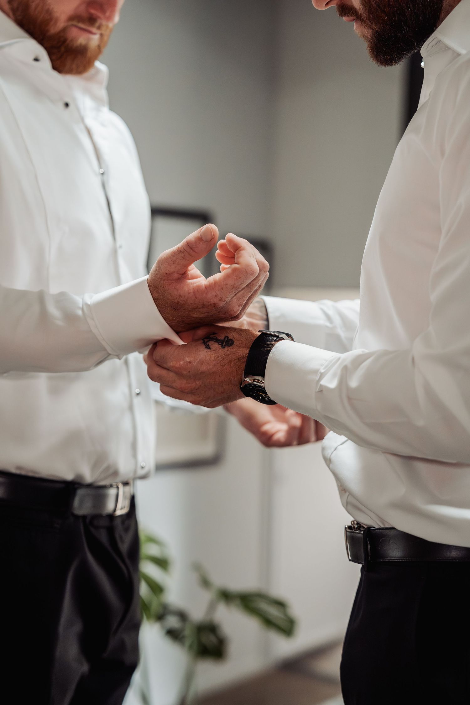 Two men in white dress shirts adjusting cufflinks before a wedding ceremony.