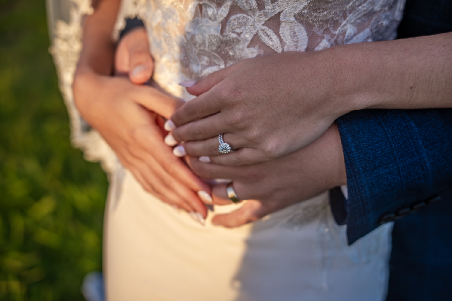 Close-up of hands showing off an engagement ring against a lace wedding dress.