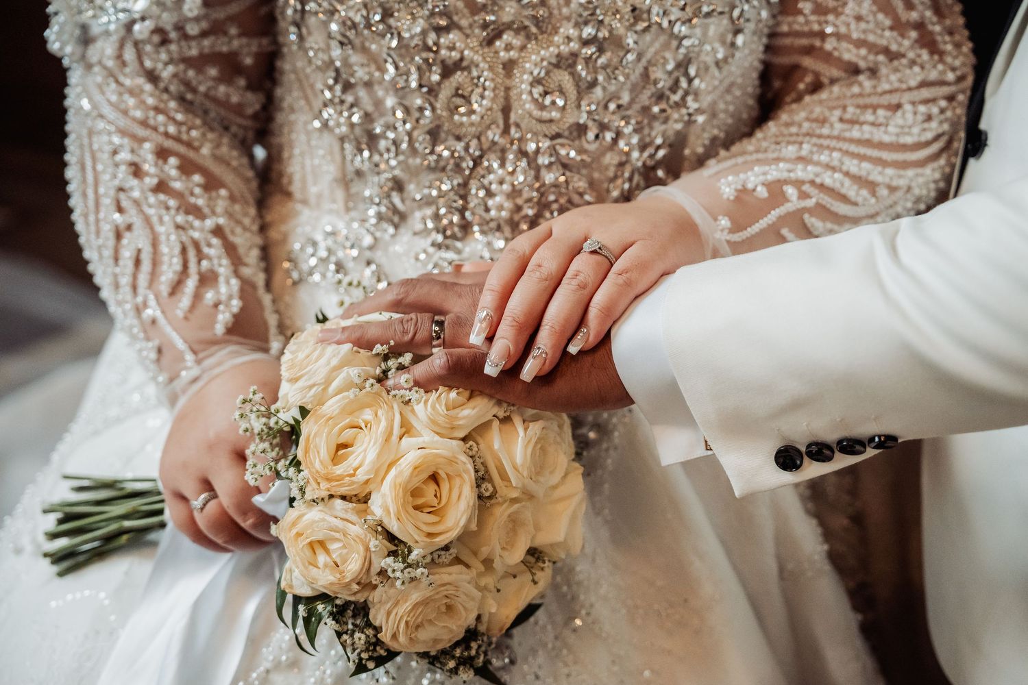 Close-up of hands holding a beautiful bouquet of cream-colored roses against white wedding attire.