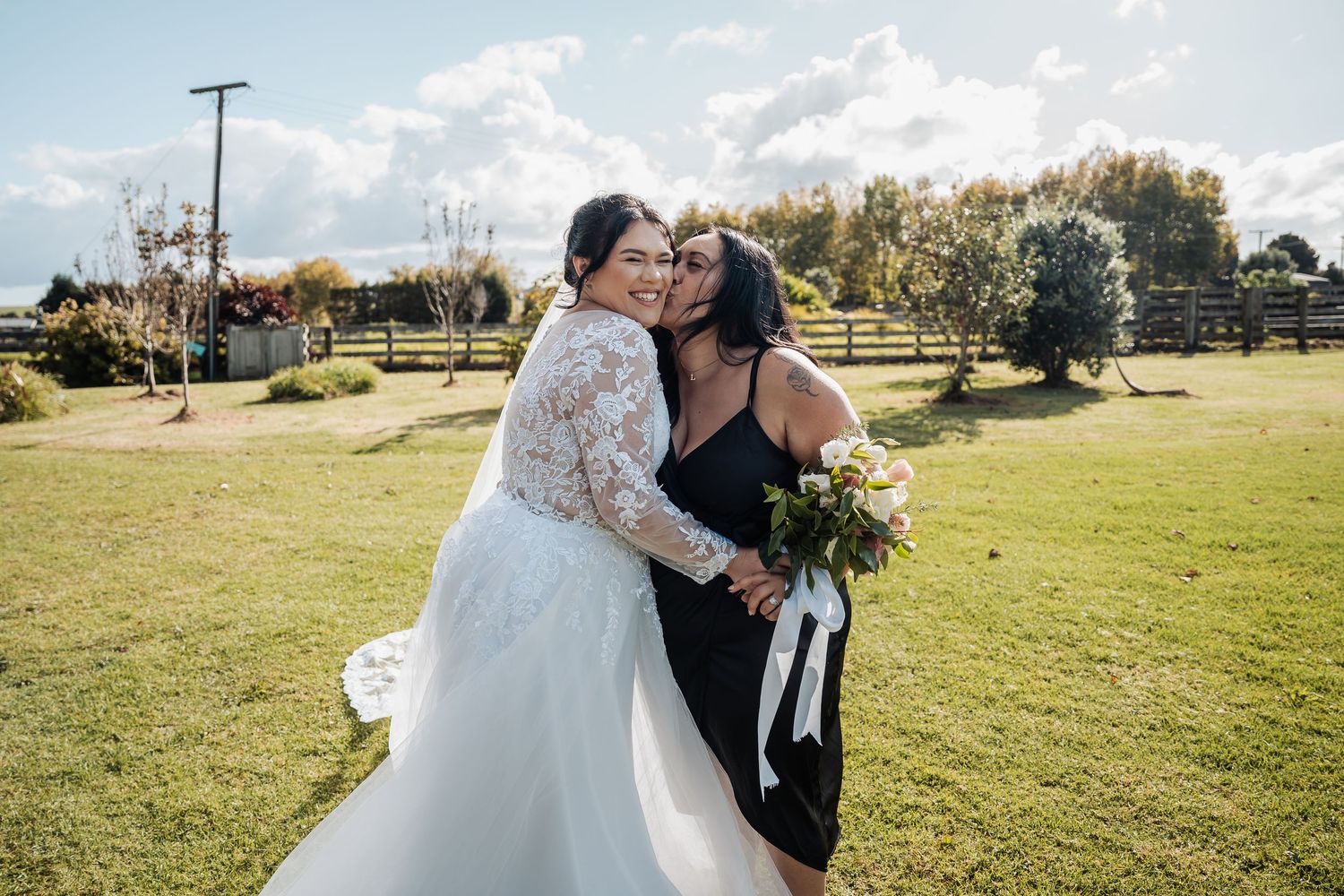 A scenic outdoor wedding celebration in a grassy field with sunshine and trees in the background.