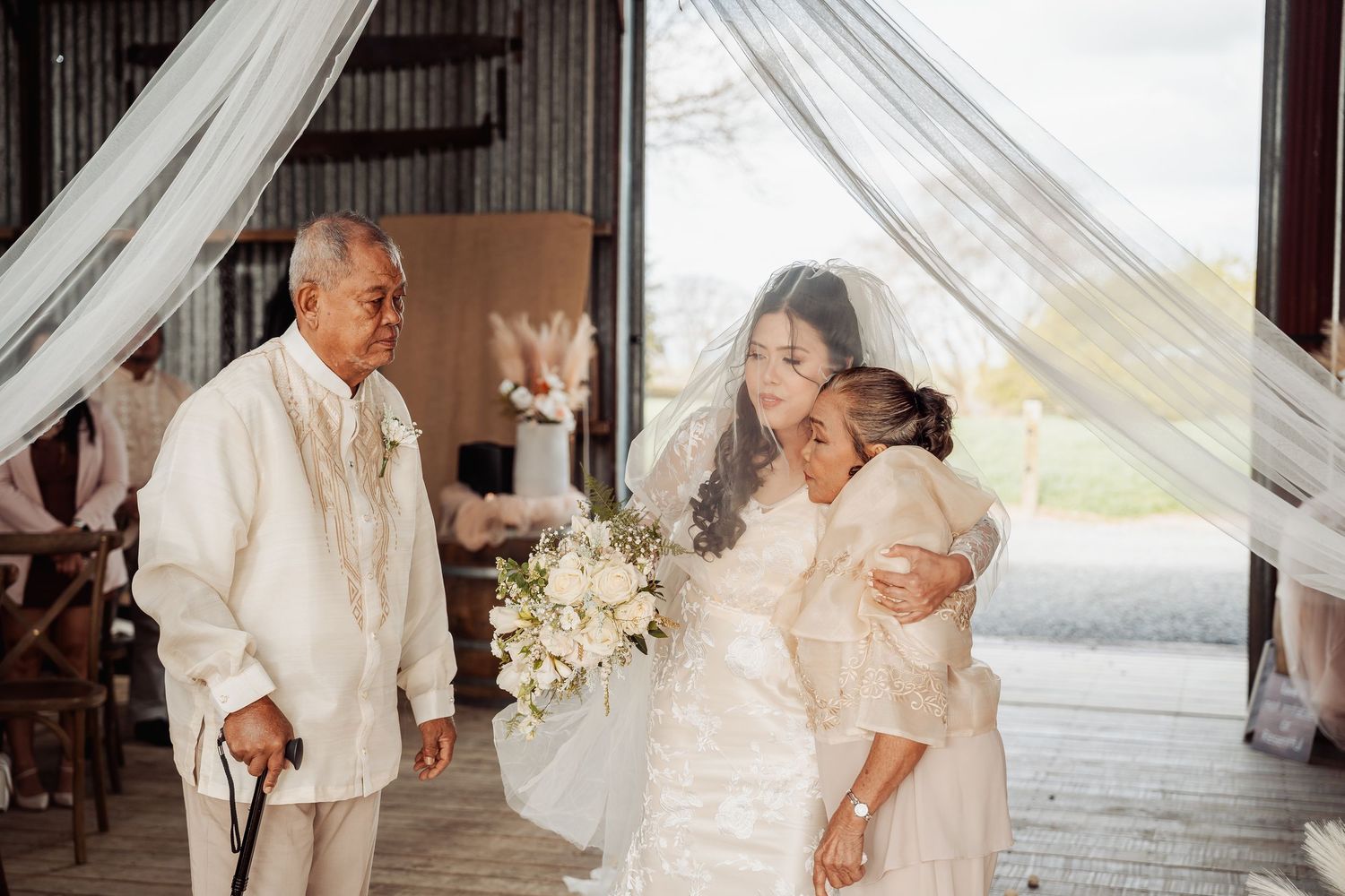 Romantic wedding moment captured in a rustic barn setting with white drapery.