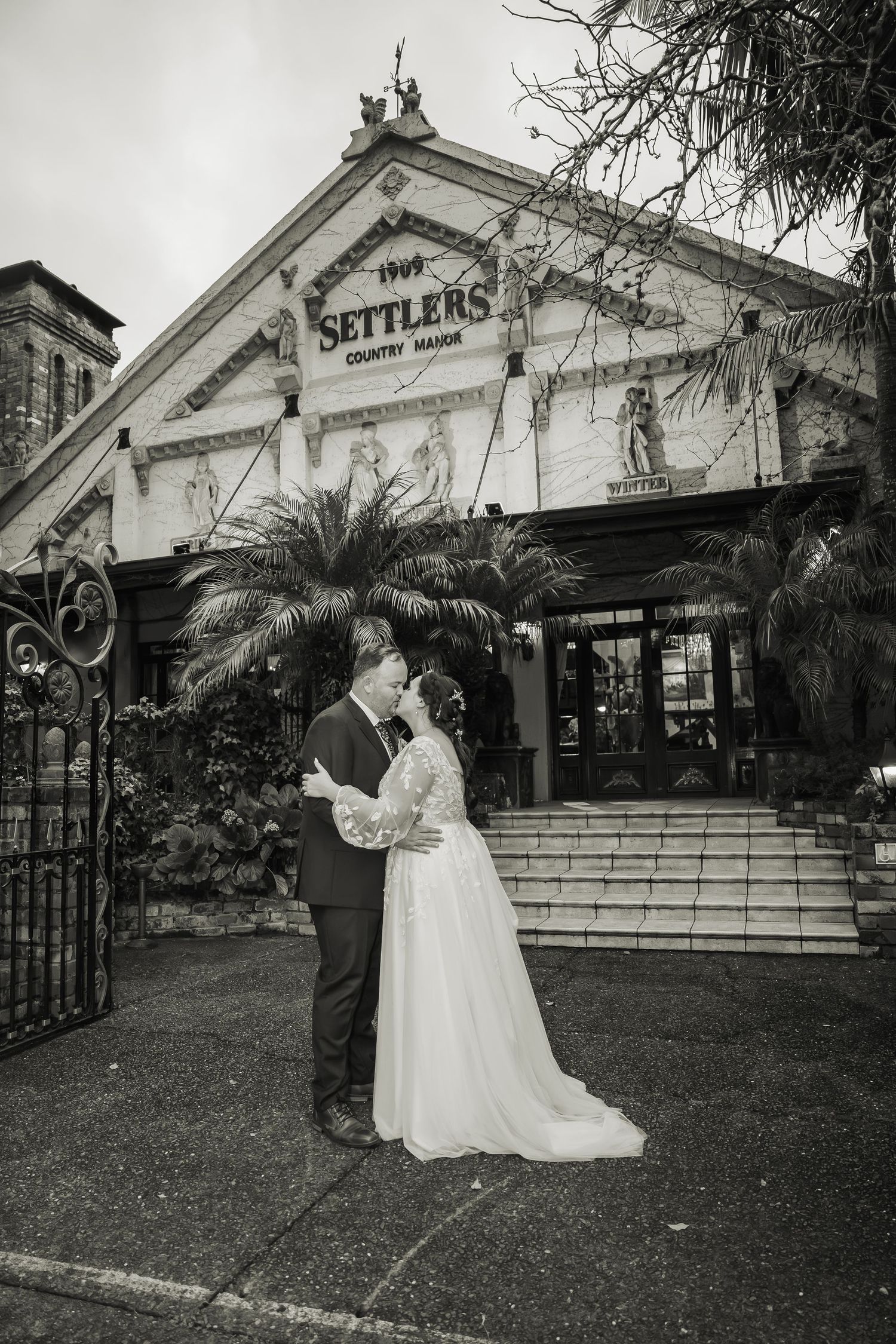 Classic wedding photography outside historic Settlers venue with wrought iron gates and palm trees.