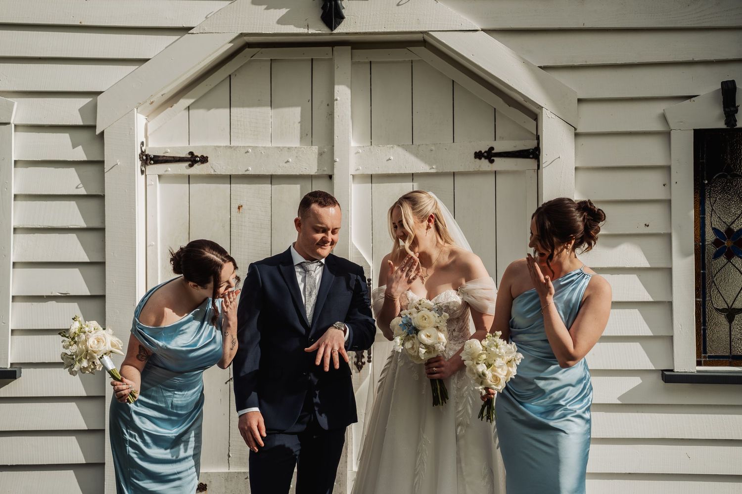 Wedding party gathered outside a classic white weatherboard building.