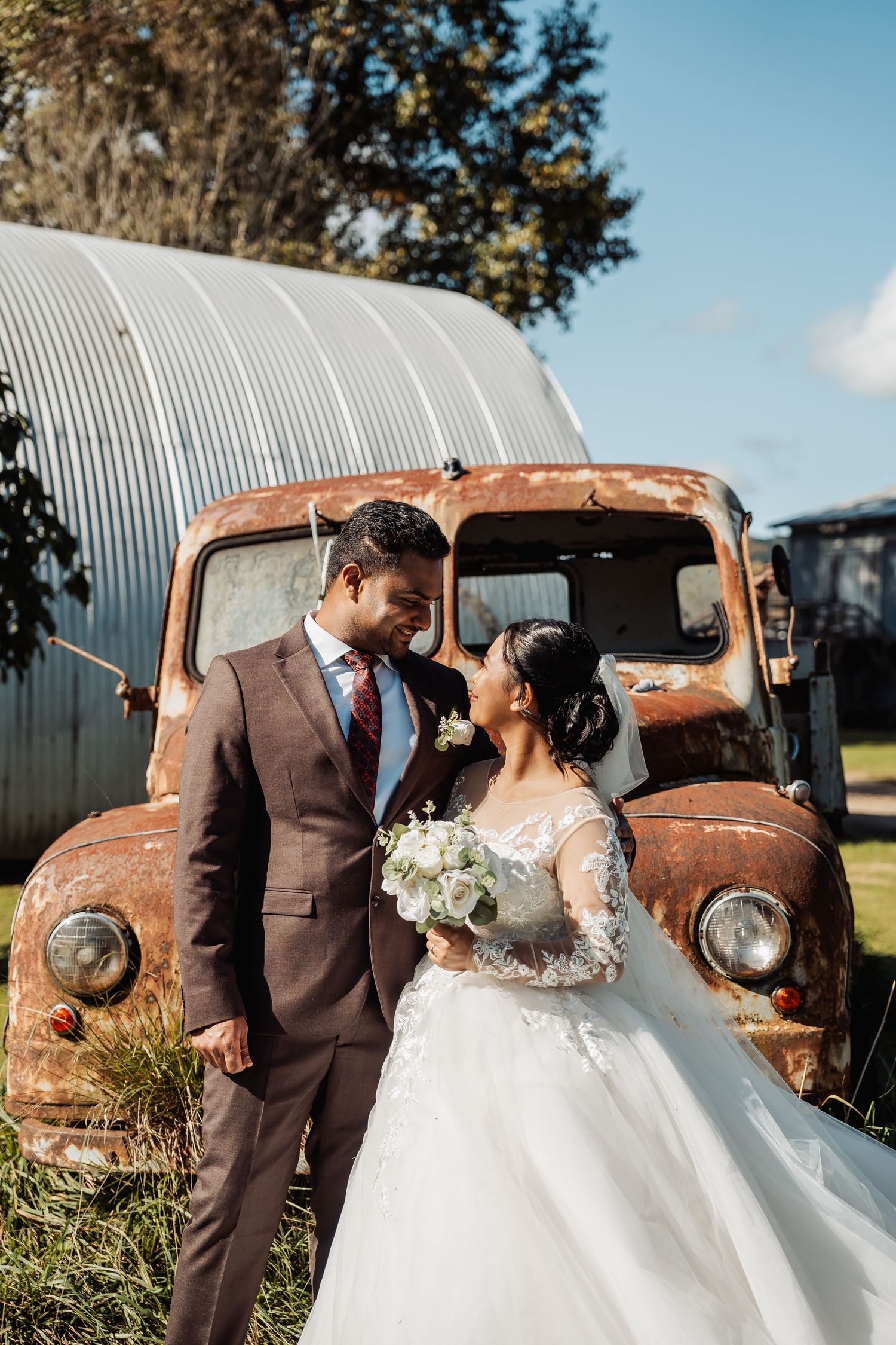 Bride and groom sharing a romantic moment beside a rustic vintage truck on their wedding day.