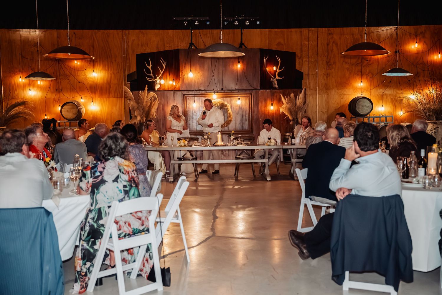 Guests seated at round tables in a warmly lit rustic barn wedding reception venue.