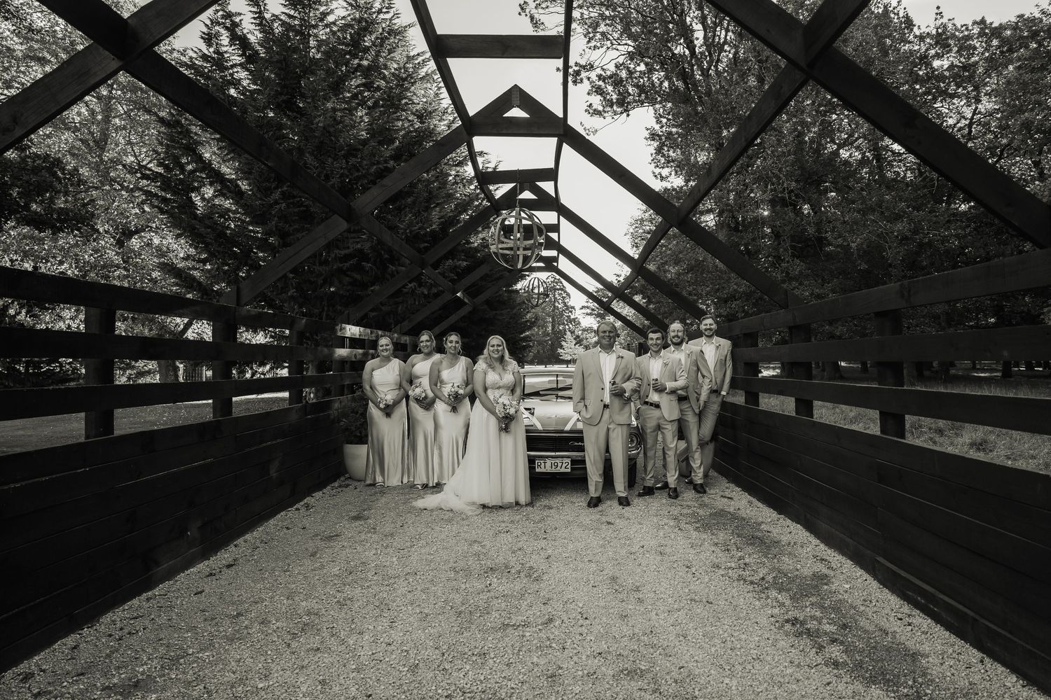 Wedding party posing in black and white photo inside rustic covered bridge venue.