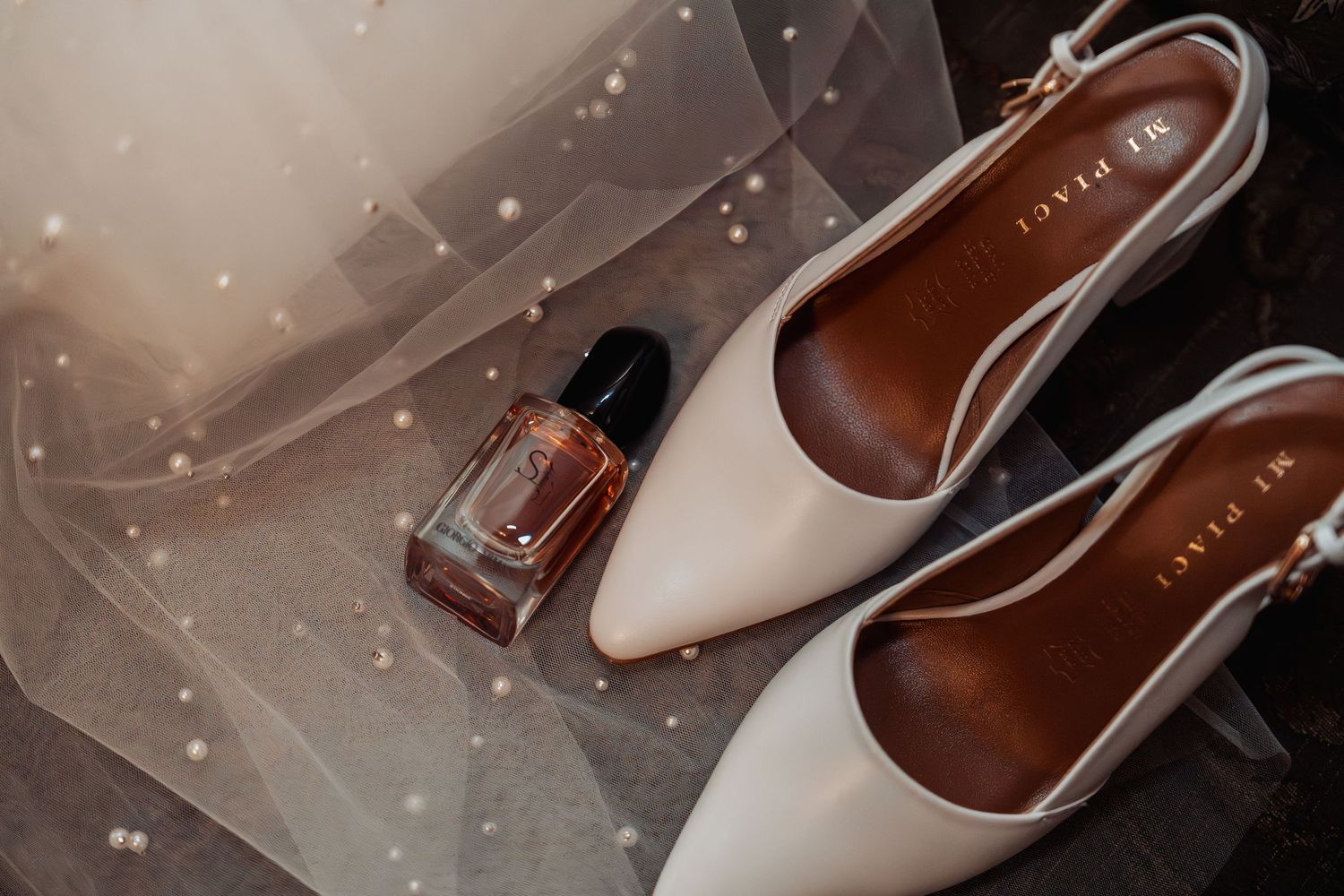 White Mi Piaci bridal heels and a perfume bottle rest on a delicate pearl-trimmed wedding veil.