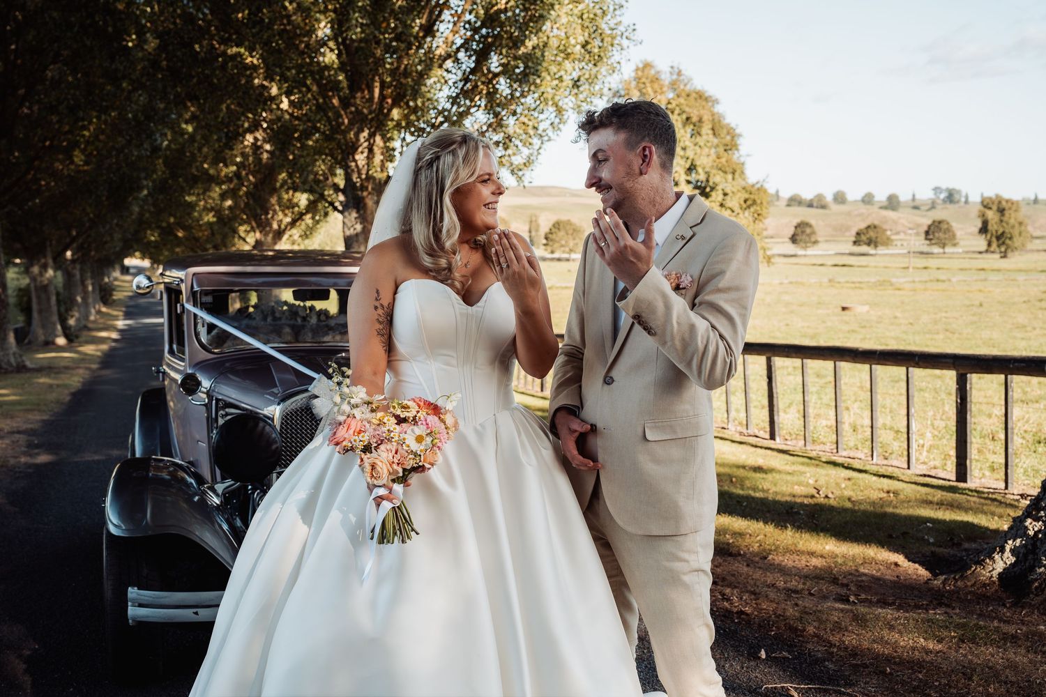 Bride and groom sharing a joyful moment beside a vintage black car on their wedding day.