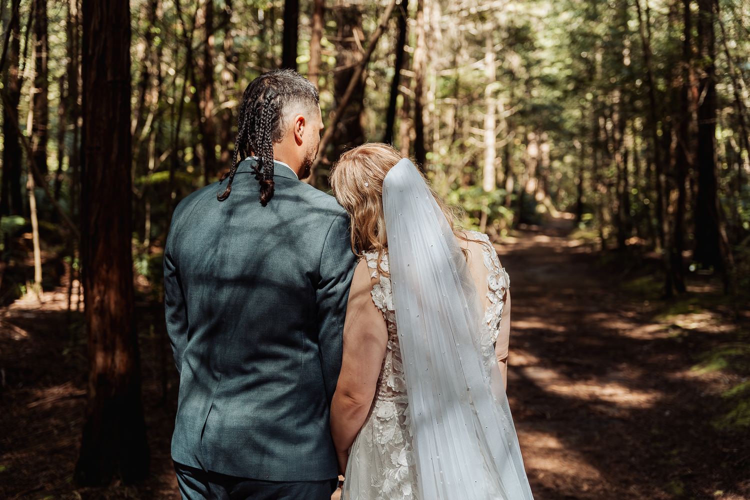 A tender moment between newlyweds walking along a forest path surrounded by majestic trees.