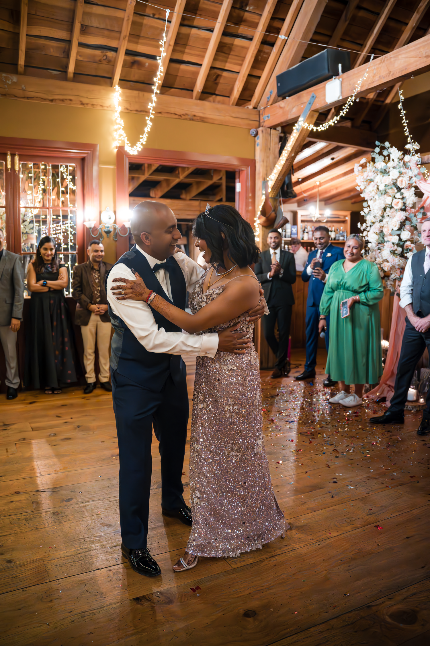Couple shares their first dance at wedding reception in rustic barn venue with string lights and wooden beams.