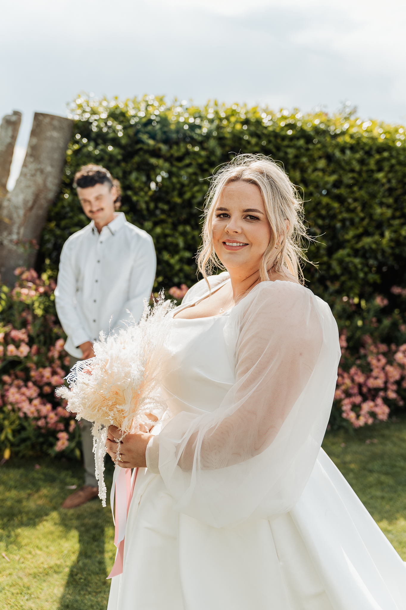Sunny garden wedding portrait with blooming flowers and manicured hedges.